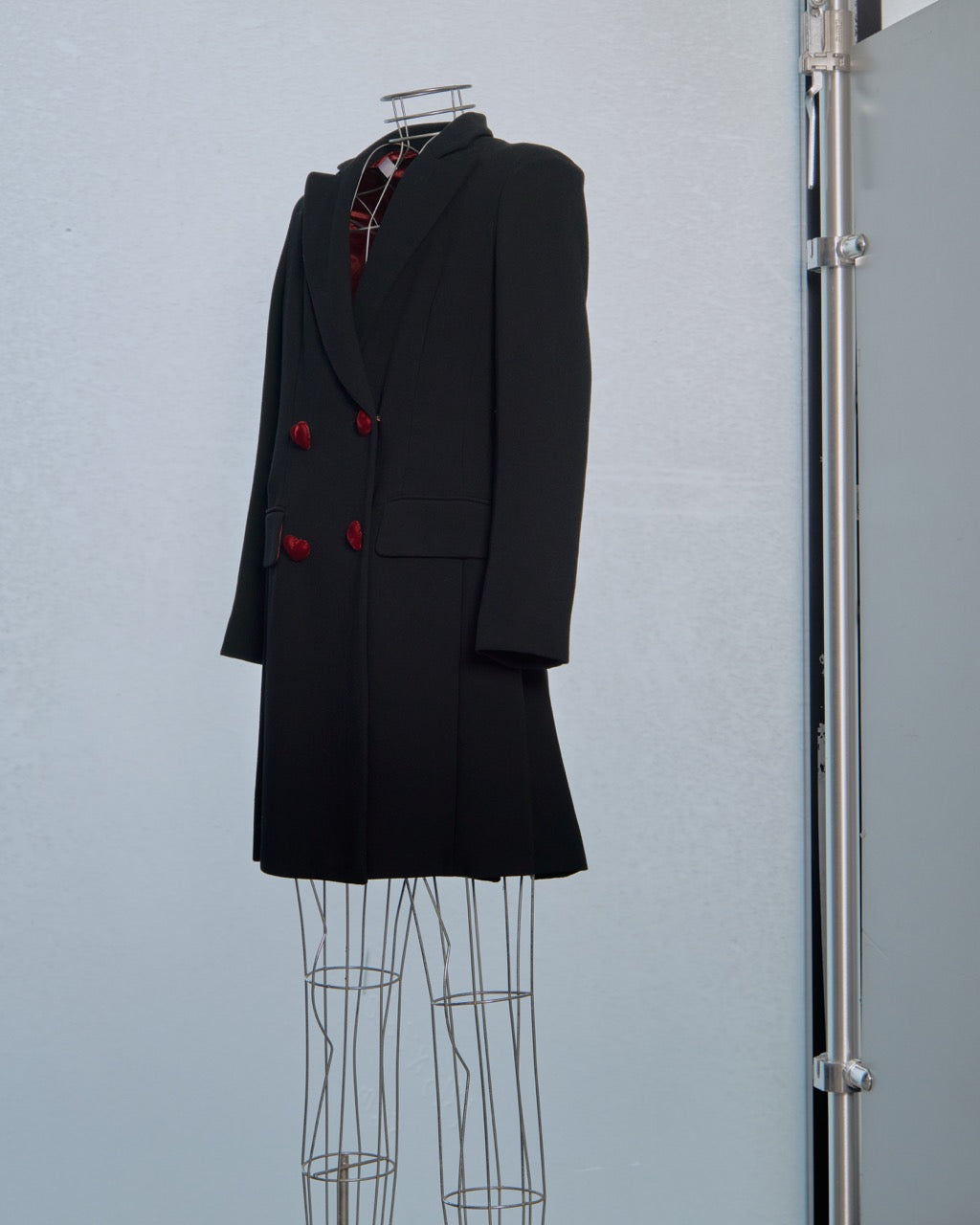 Black Moschino coat with red heart buttons on a mannequin against a light blue wall.