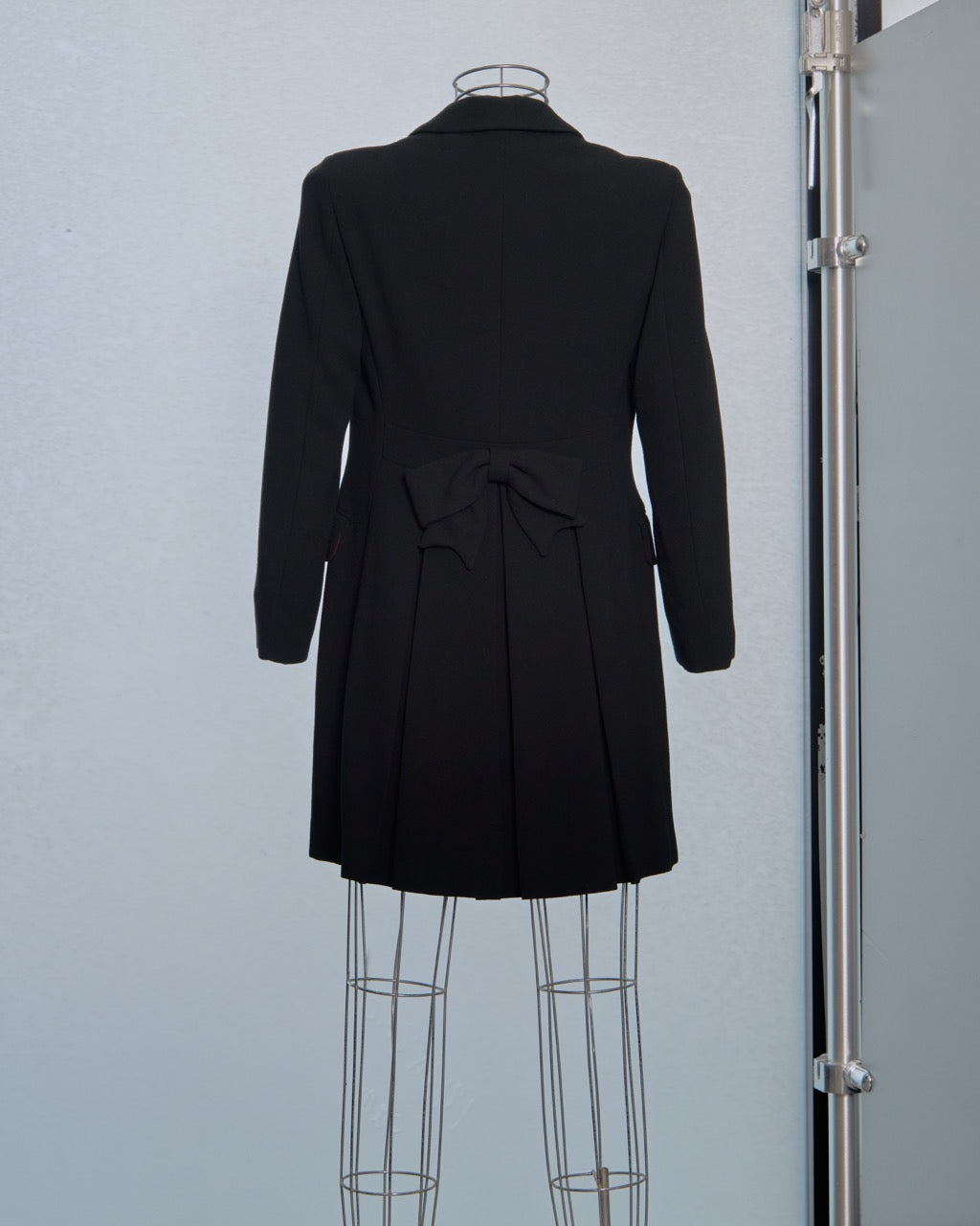 Black Moschino coat on a mannequin against a plain background