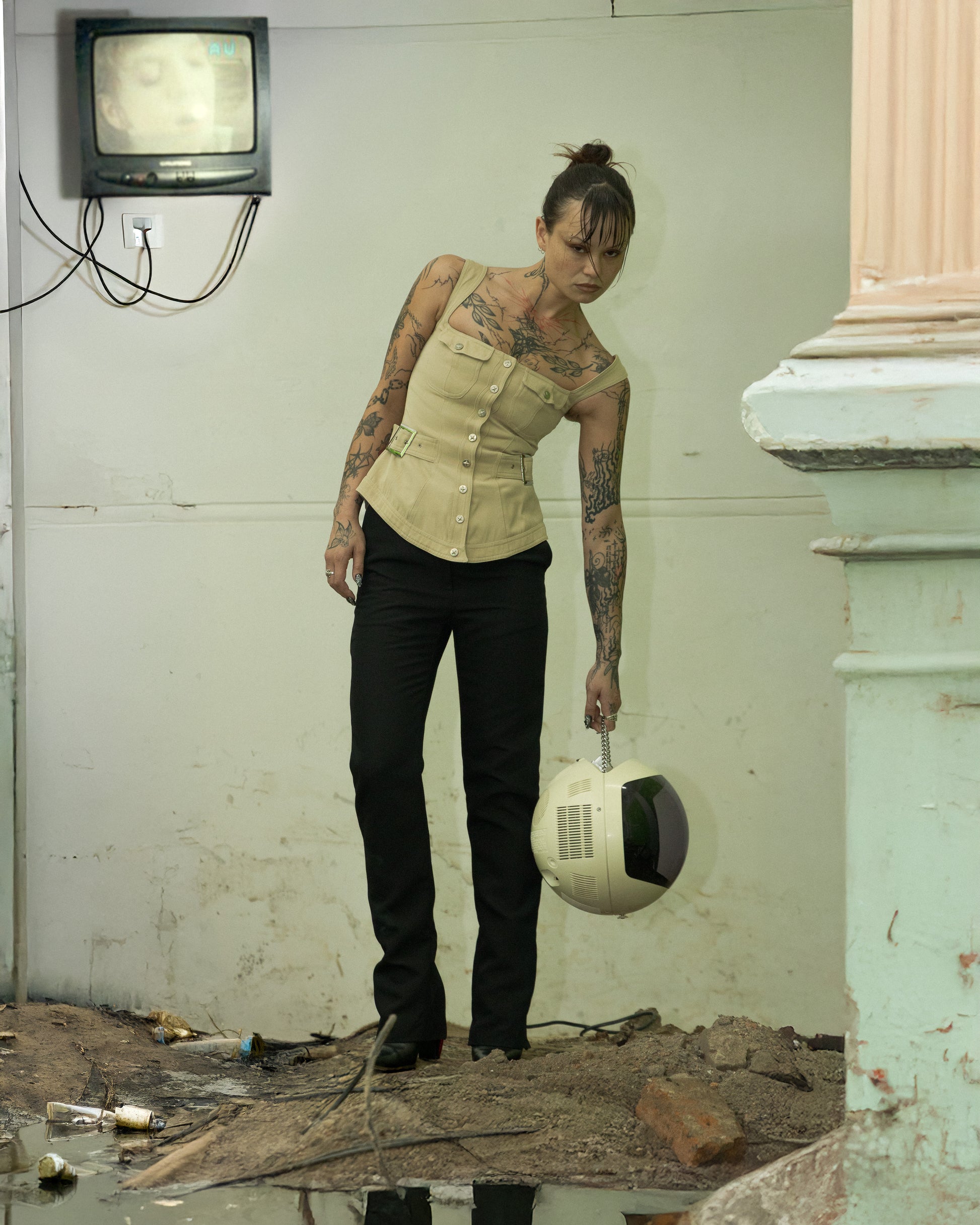 A person standing in a dilapidated room holding a white Mugler bustier with a press-stud front.