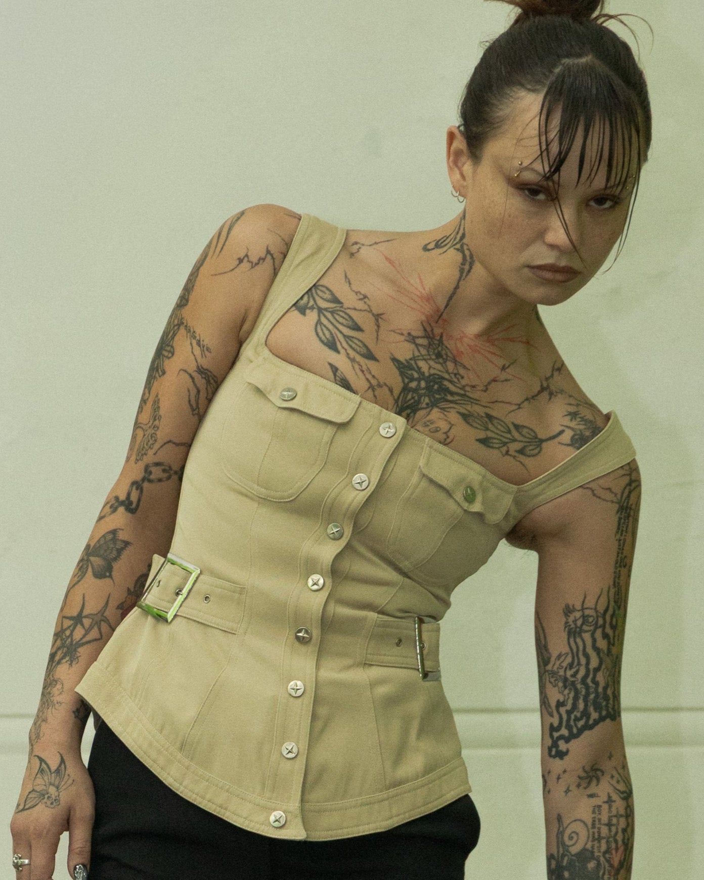 Woman wearing a beige Mugler vest with tattoos on her arms and neck against a plain background