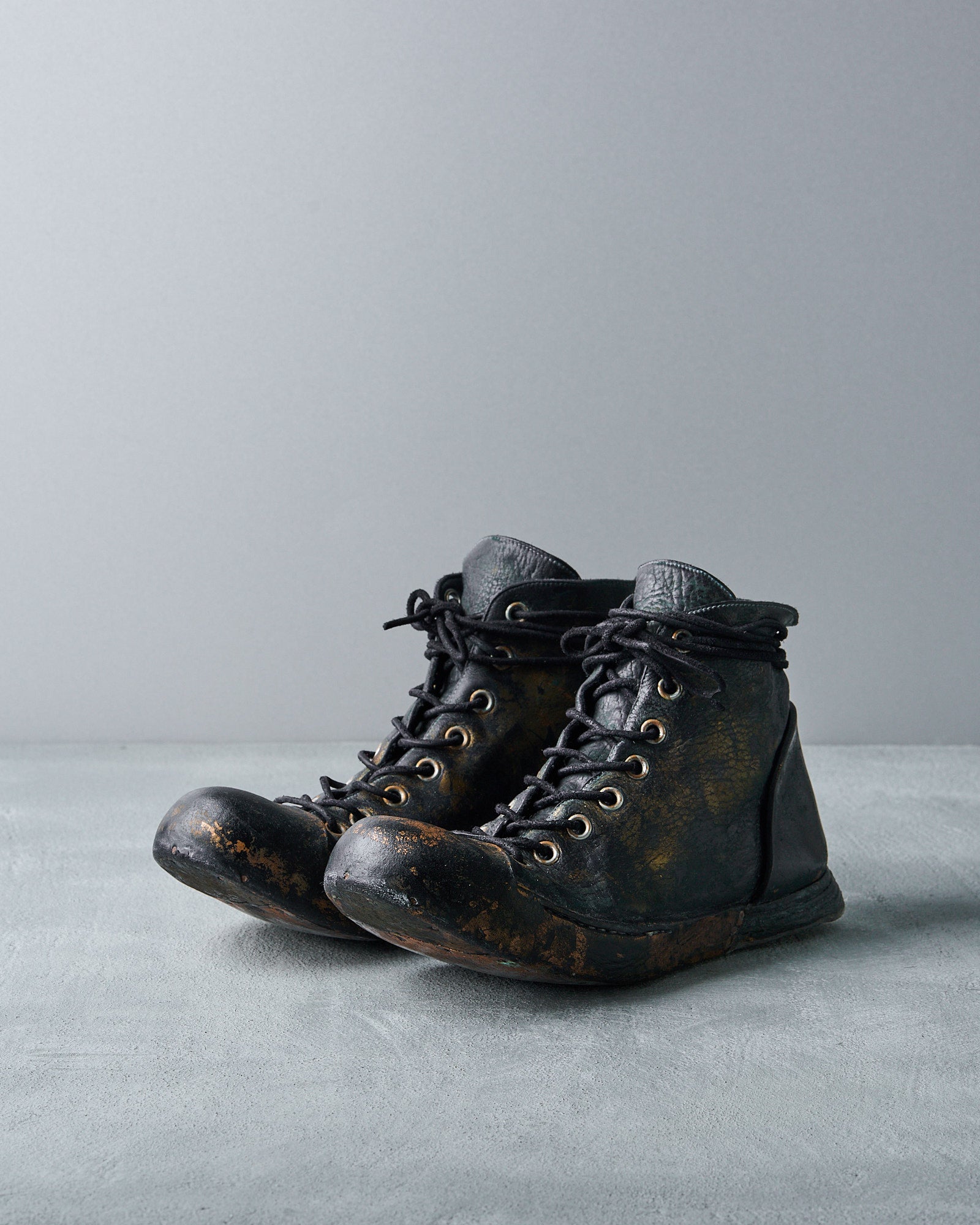 A pair of black, bespoke, high-top Nihomano leather boots with copper leaf finishing and a tonal rubber sole, displayed against a grey background.