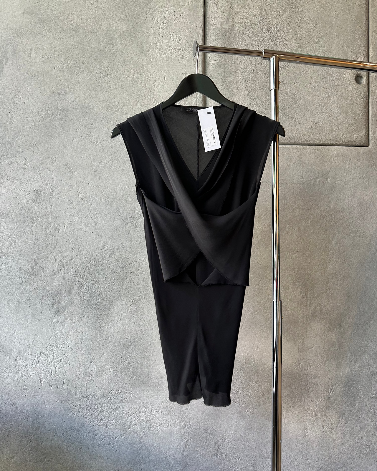 Black sleeveless P.R.Patterson top hanging on a rack against a textured wall.