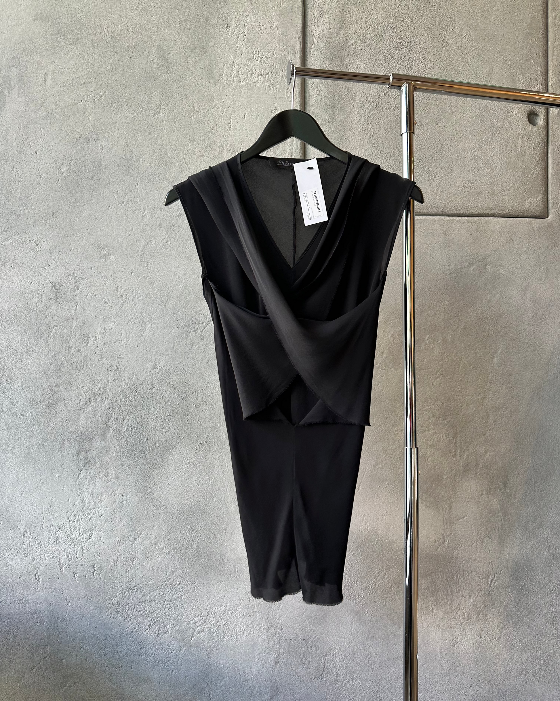 Black sleeveless P.R.Patterson wrap top on a hanger against a gray wall