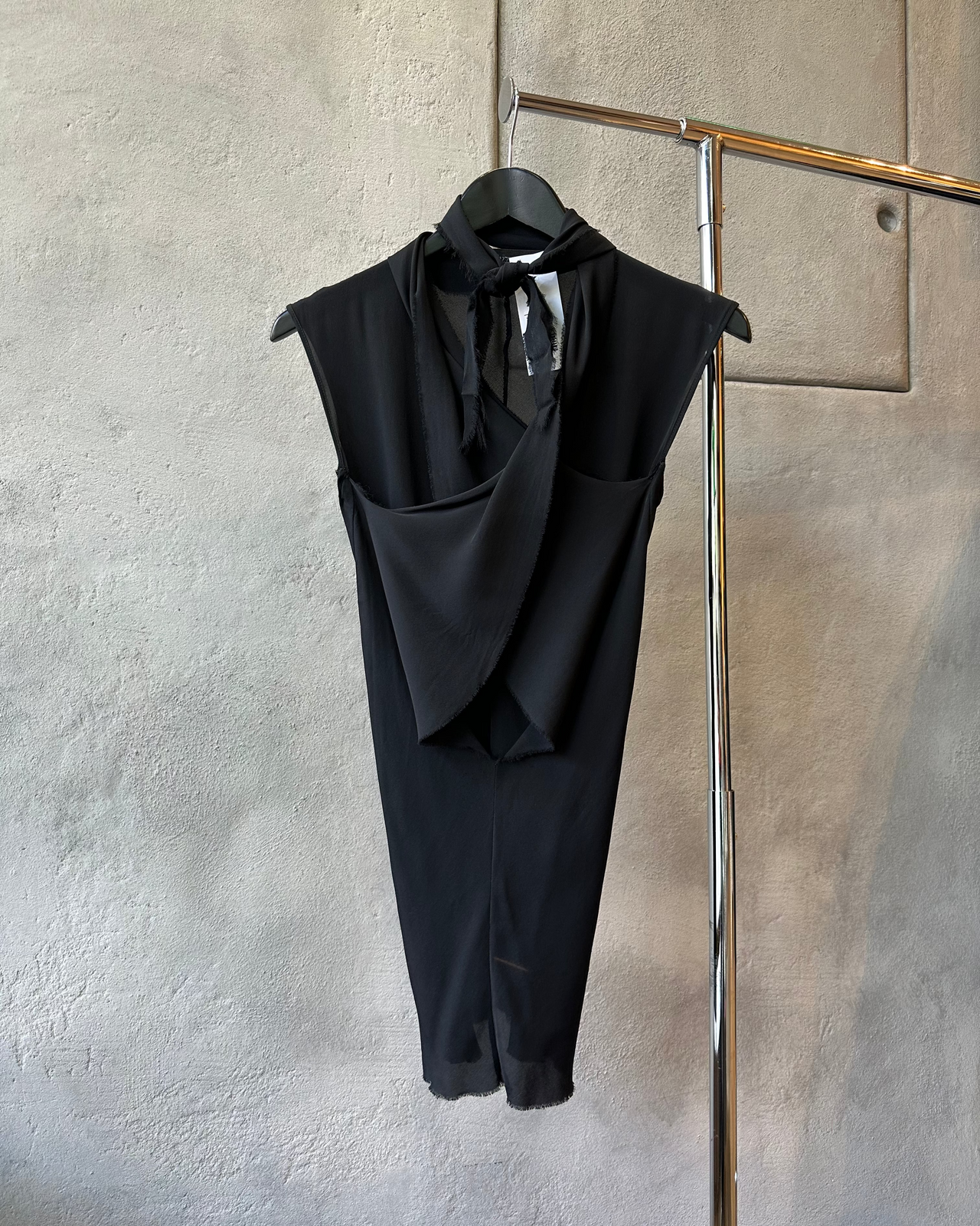 Black sleeveless P.R.Patterson top hanging on a rack against a textured wall.