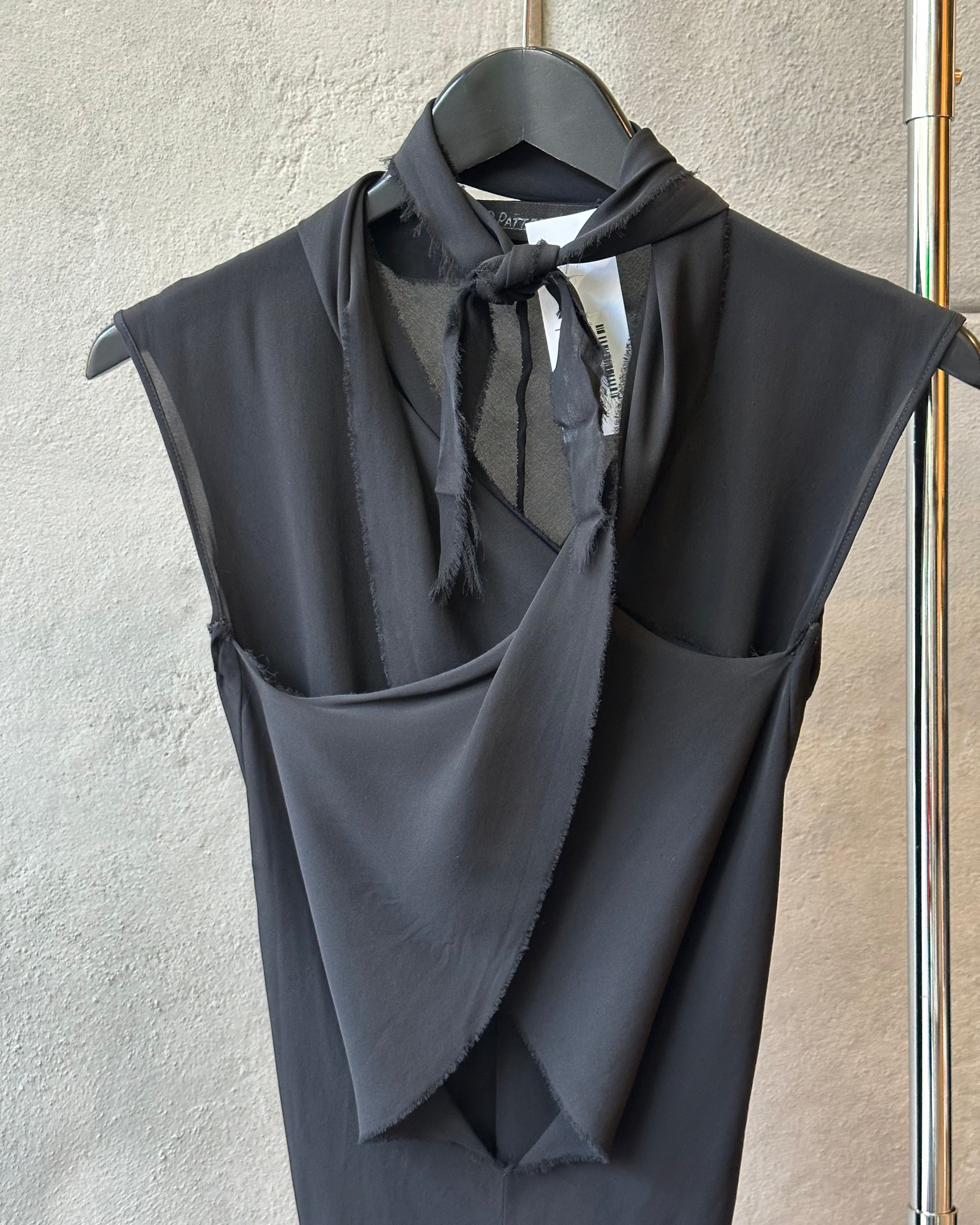 Black sleeveless P.R.Patterson top with a scarf on a hanger against a neutral wall.