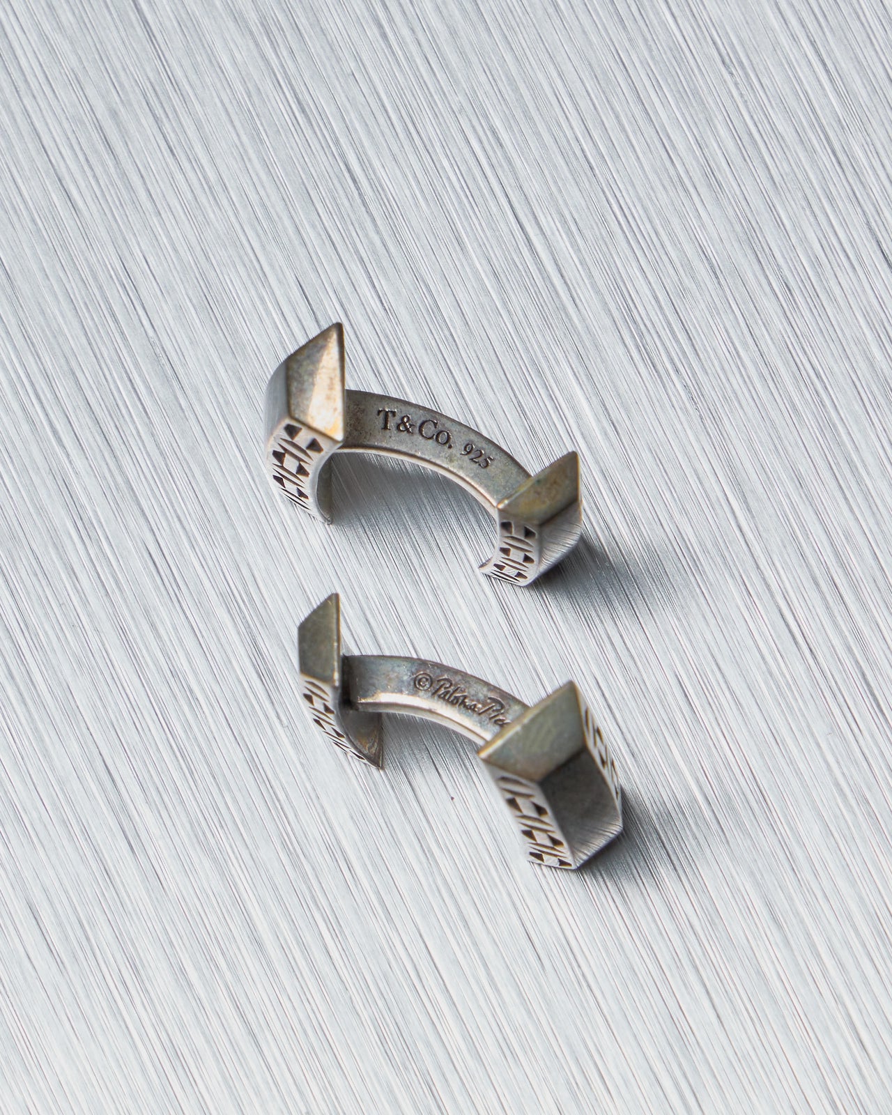 Silver open-style Tiffany and Co cufflinks on a textured gray background