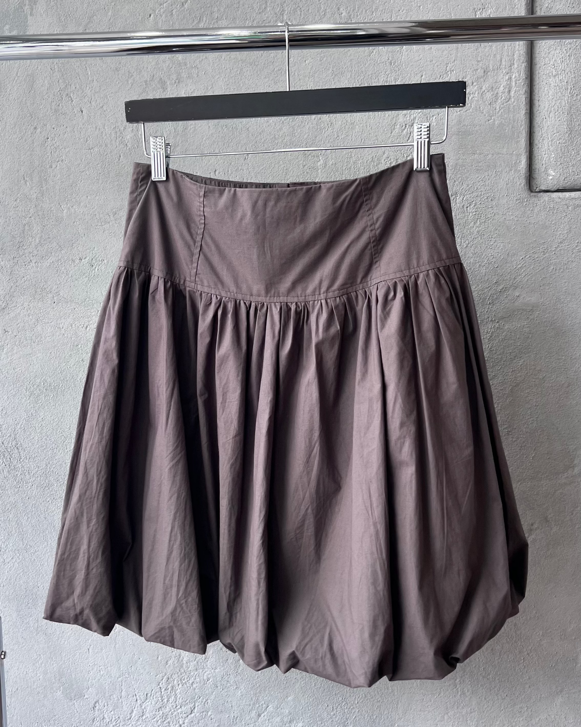 Brown Paloma Wool skirt hanging on a rack against a gray wall