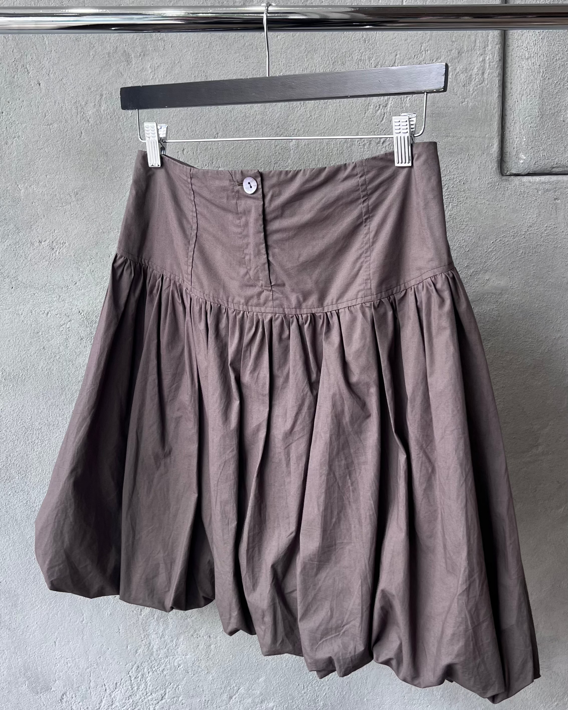 Brown Paloma Wool skirt hanging on a rack against a gray wall