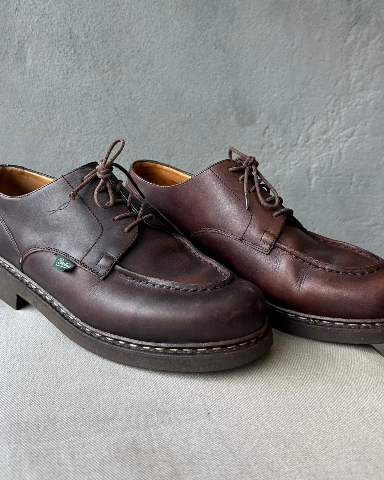 Pair of brown leather Paraboot shoes on a textured concrete floor with a gray wall background