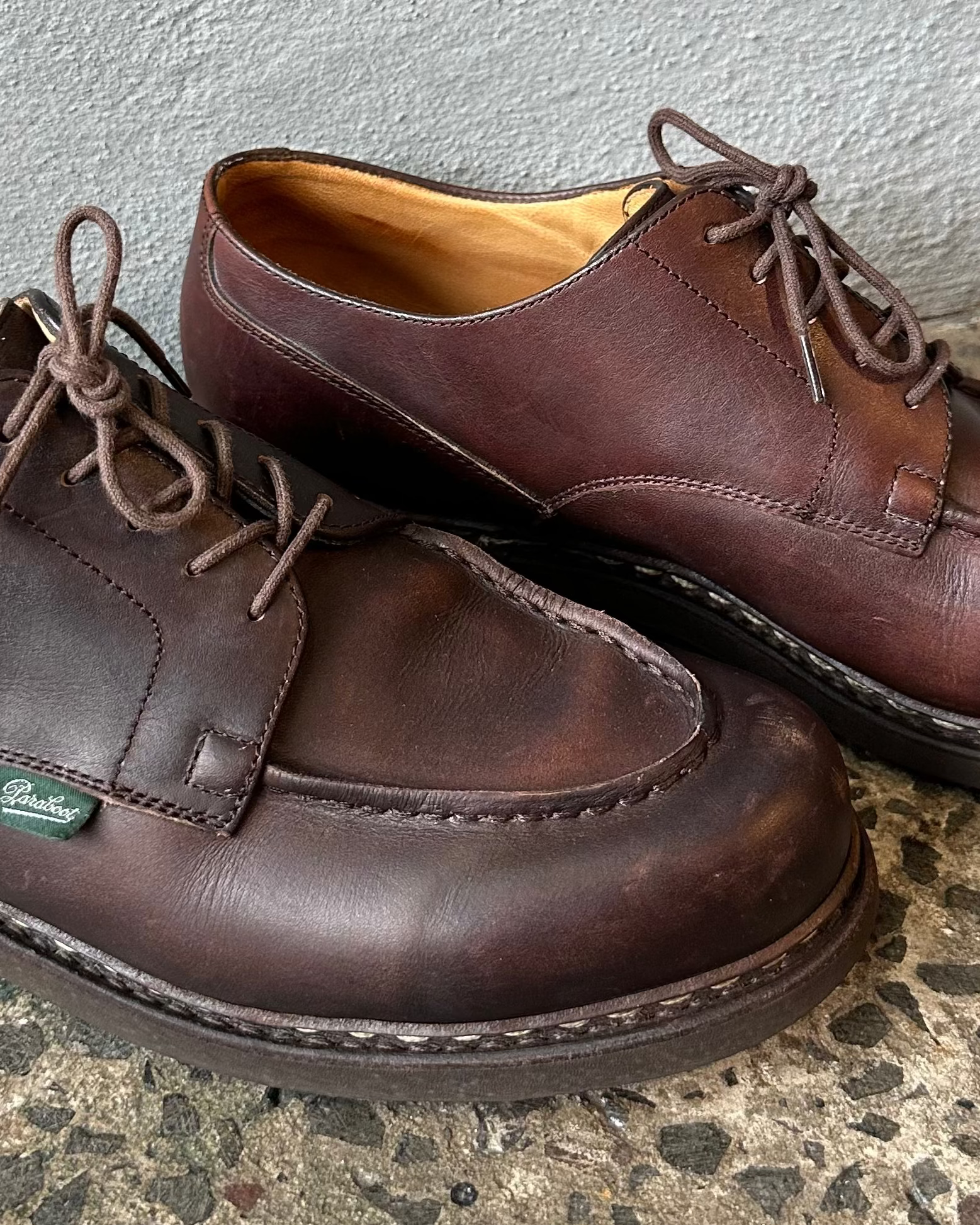 Pair of brown leather Paraboot shoes on a textured surface with a gray background