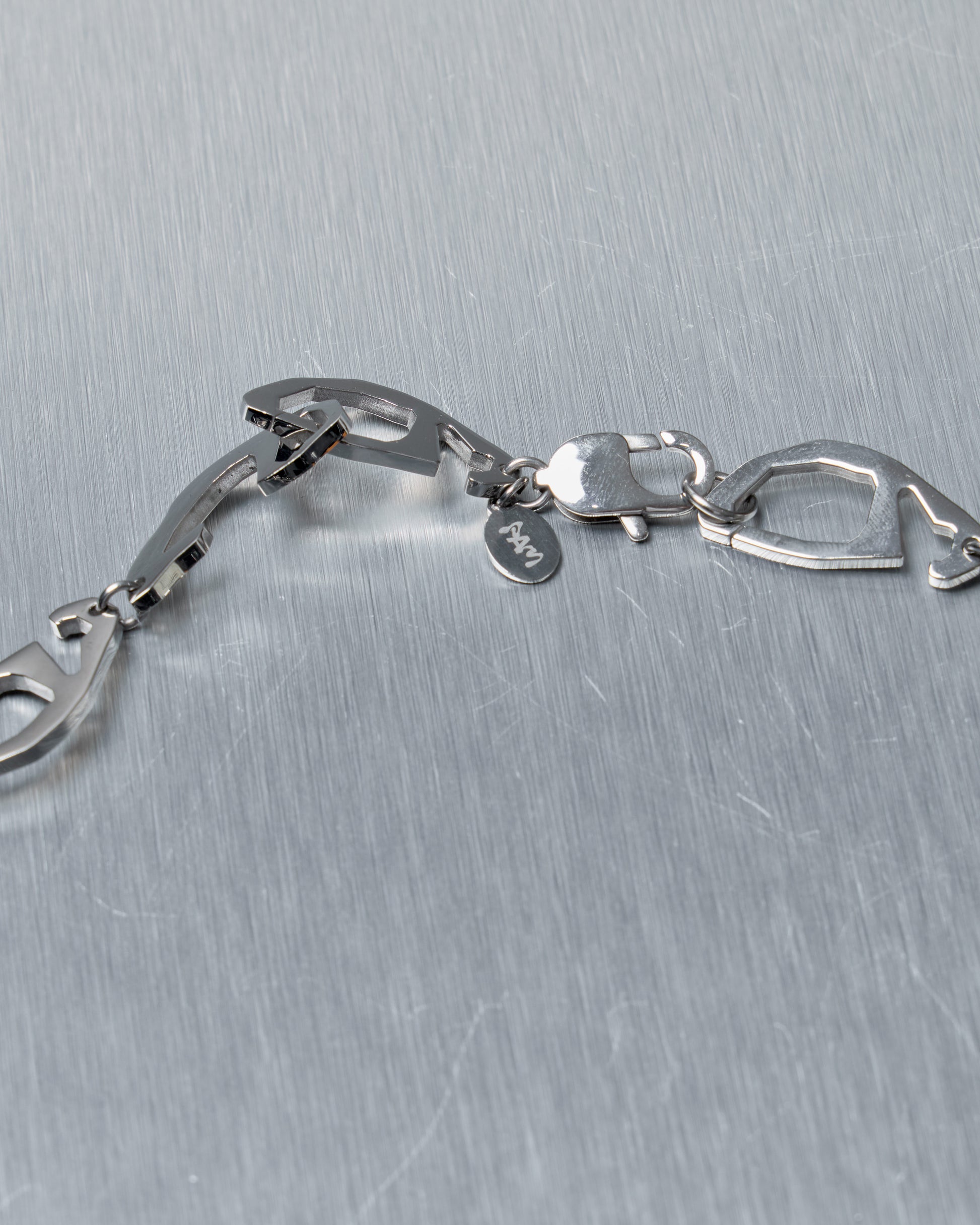 Close-up of a silver Perks and Mini necklace on a metallic surface