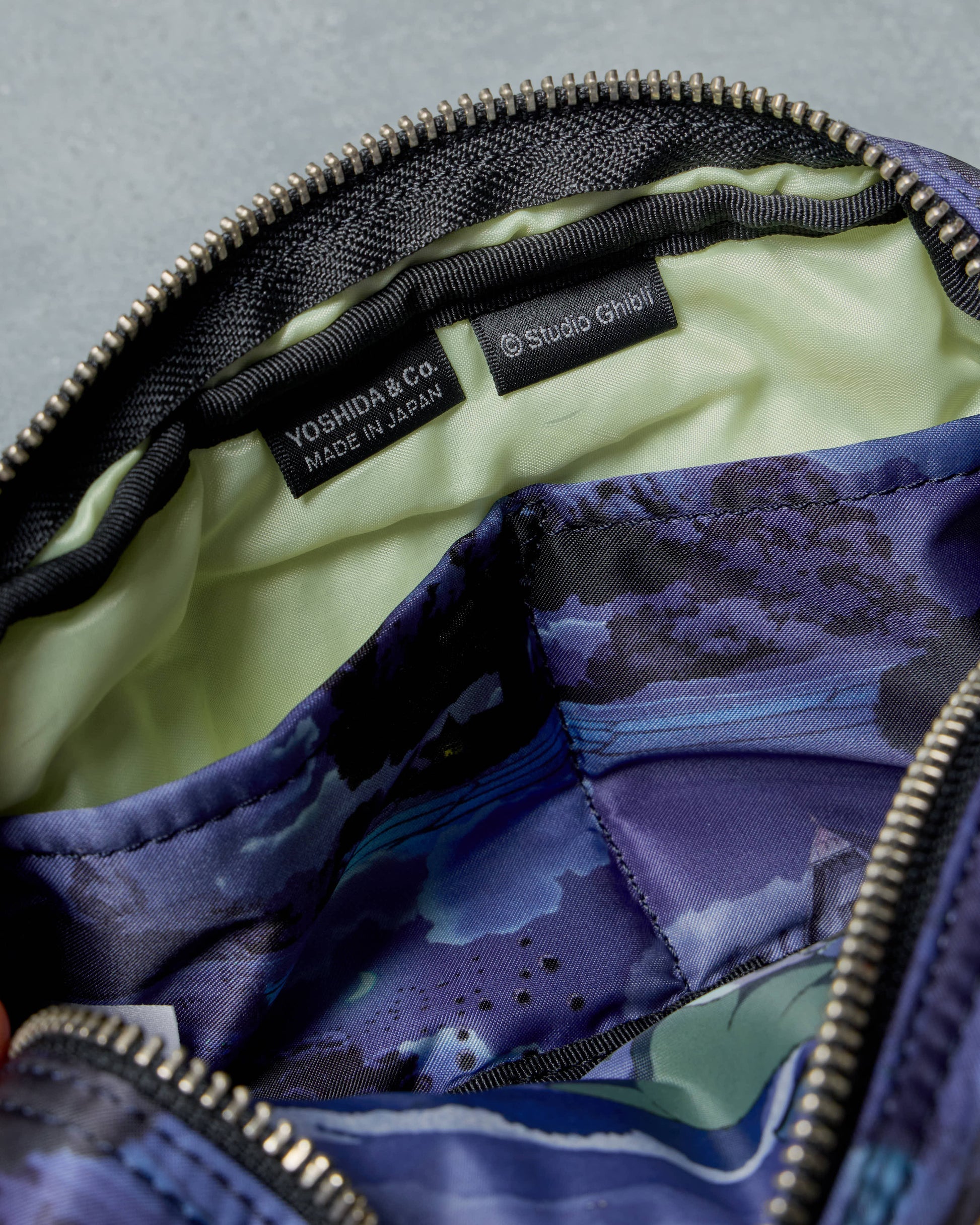 Close-up of a purple camouflage Porter x Ghibli Totoro bag with 'Yoshida & Co.' and 'Studio Ghibli' labels.