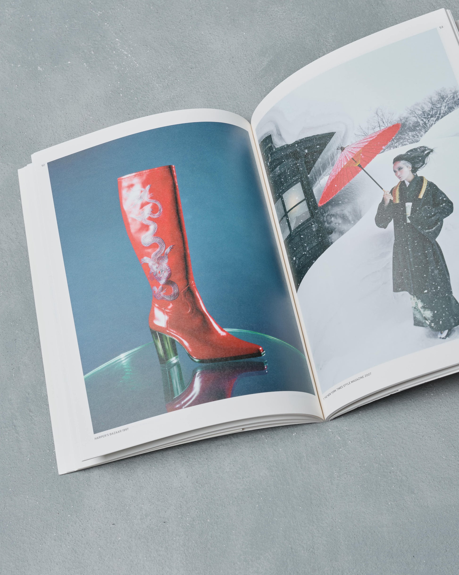 Open Ppaper Magazine showing a red boot on one page and a person with an umbrella in the snow on the other, on a gray surface.