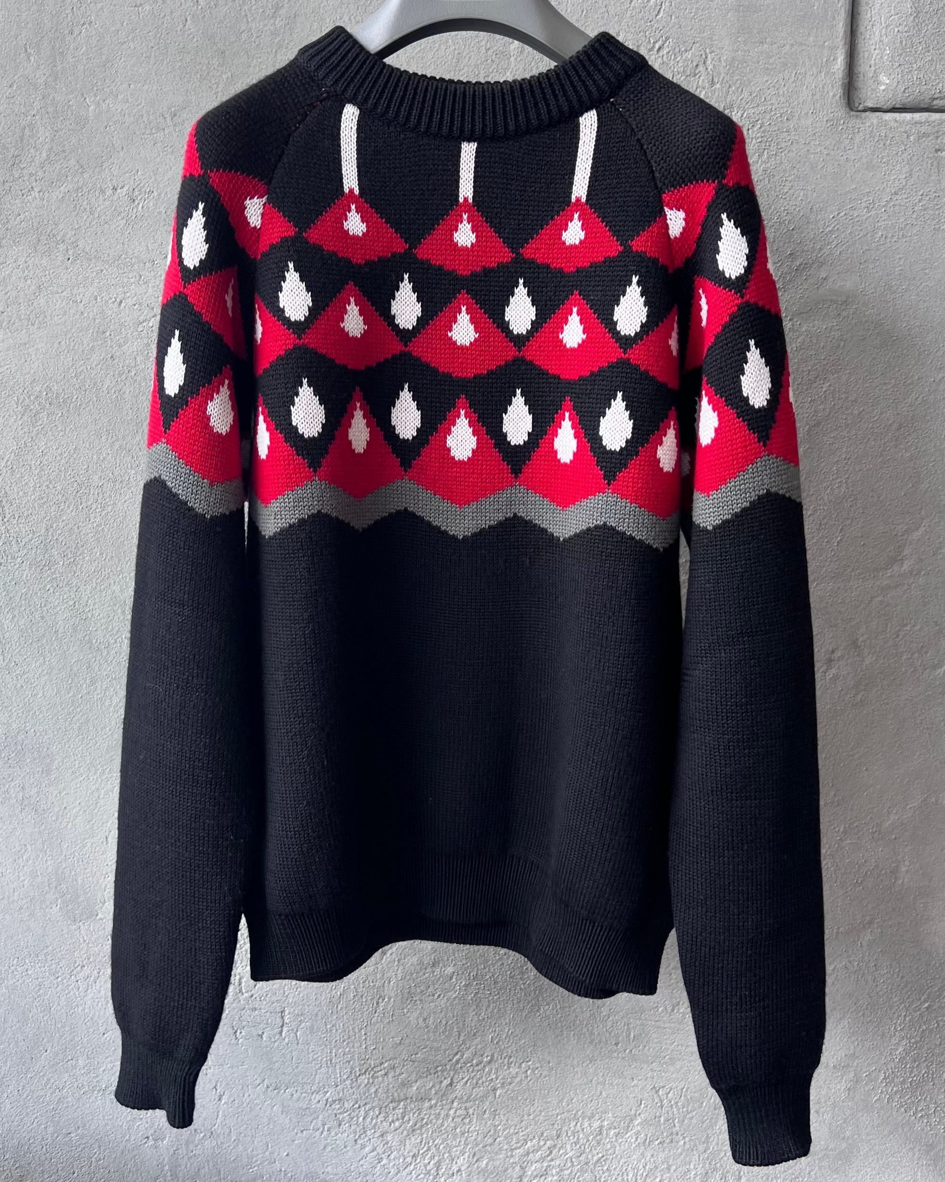 Black Prada sweater with red and white pattern hanging on a gray wall