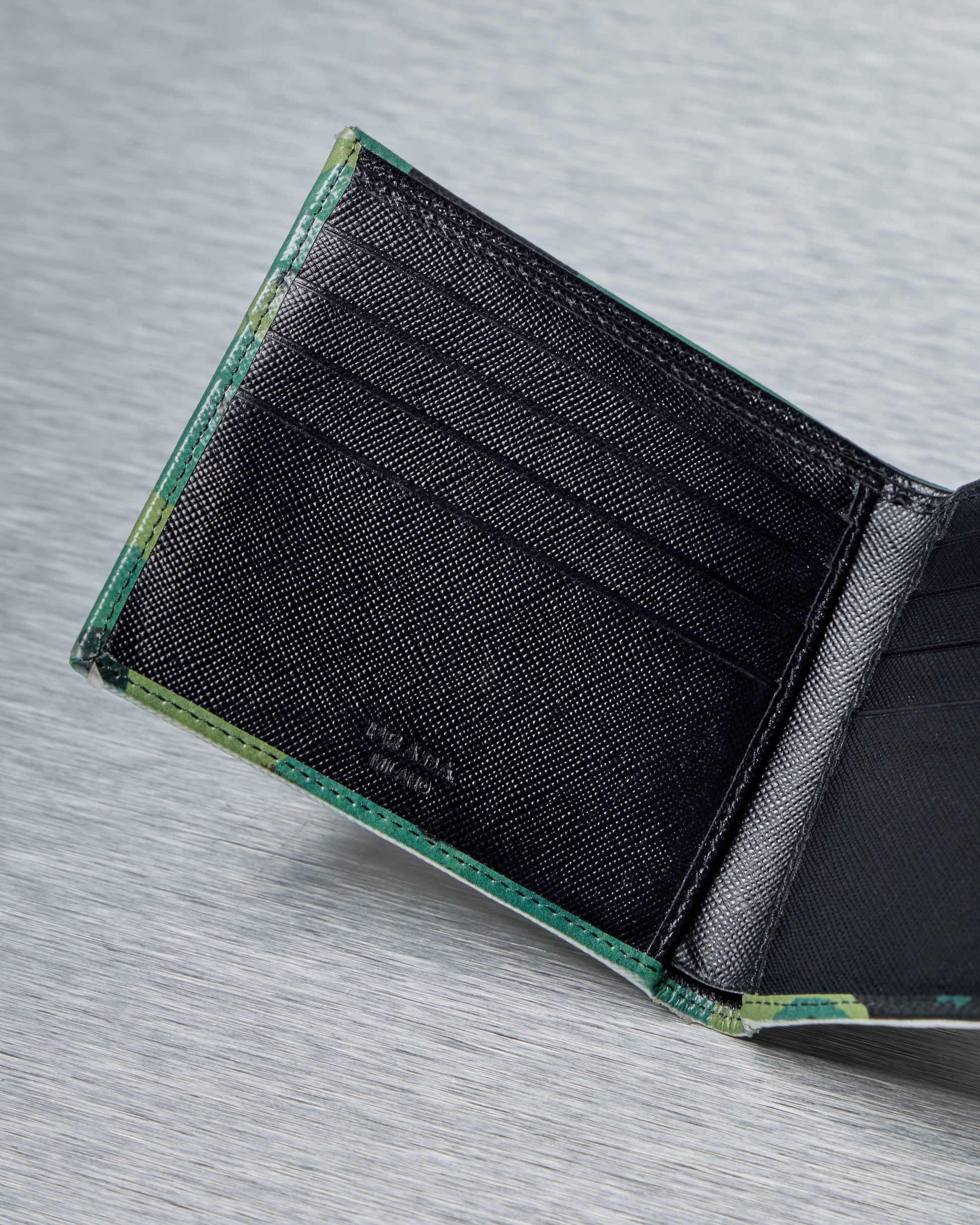 Black inside of Prada wallet with green edge on a gray textured surface