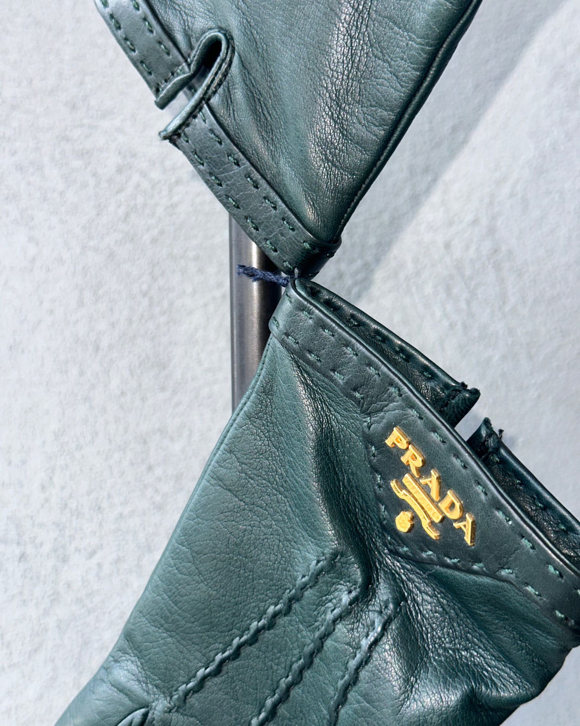 Close-up of green leather glove with Prada logo on a light gray background