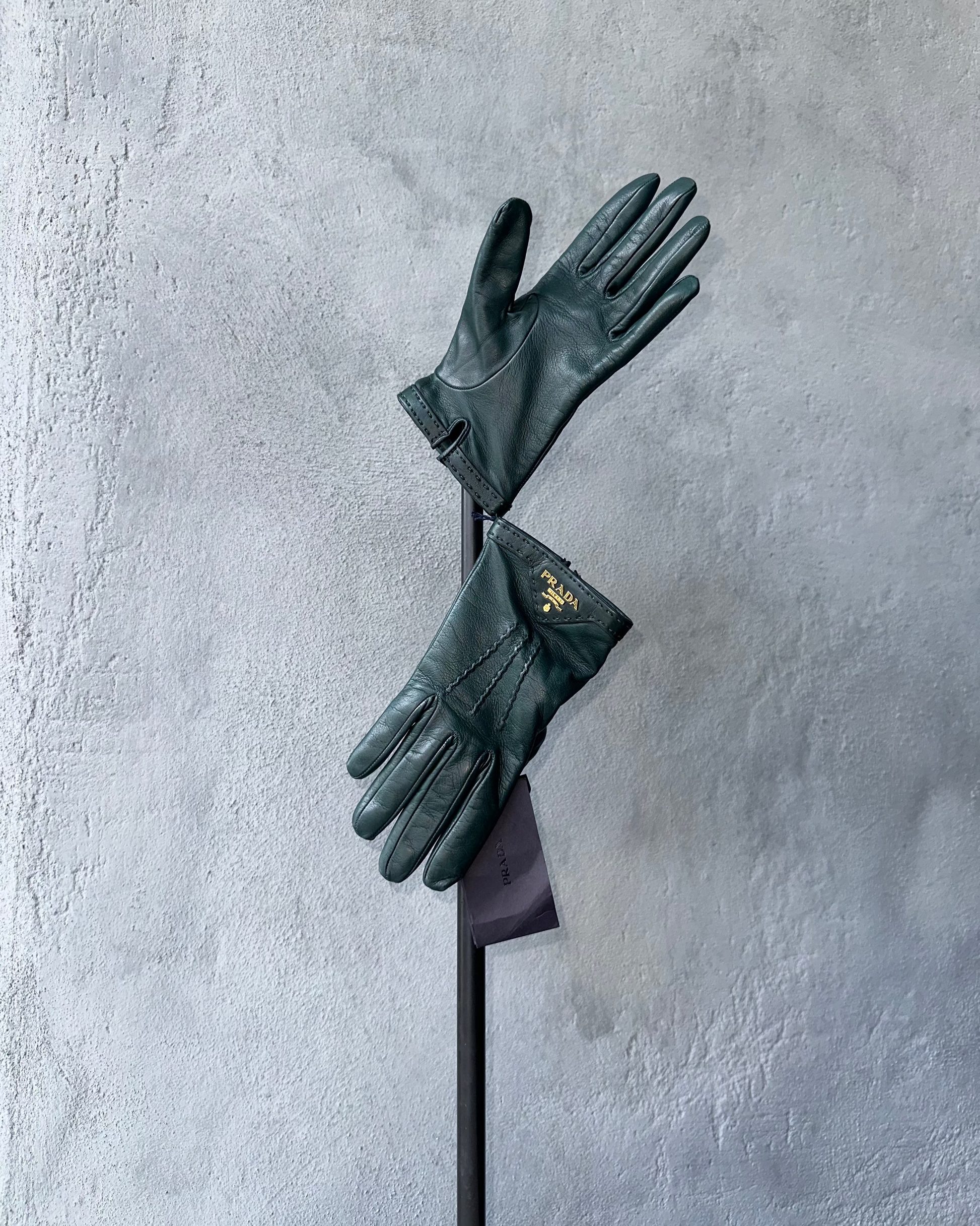 Pair of dark Prada green gloves with a brand logo on a gray textured background