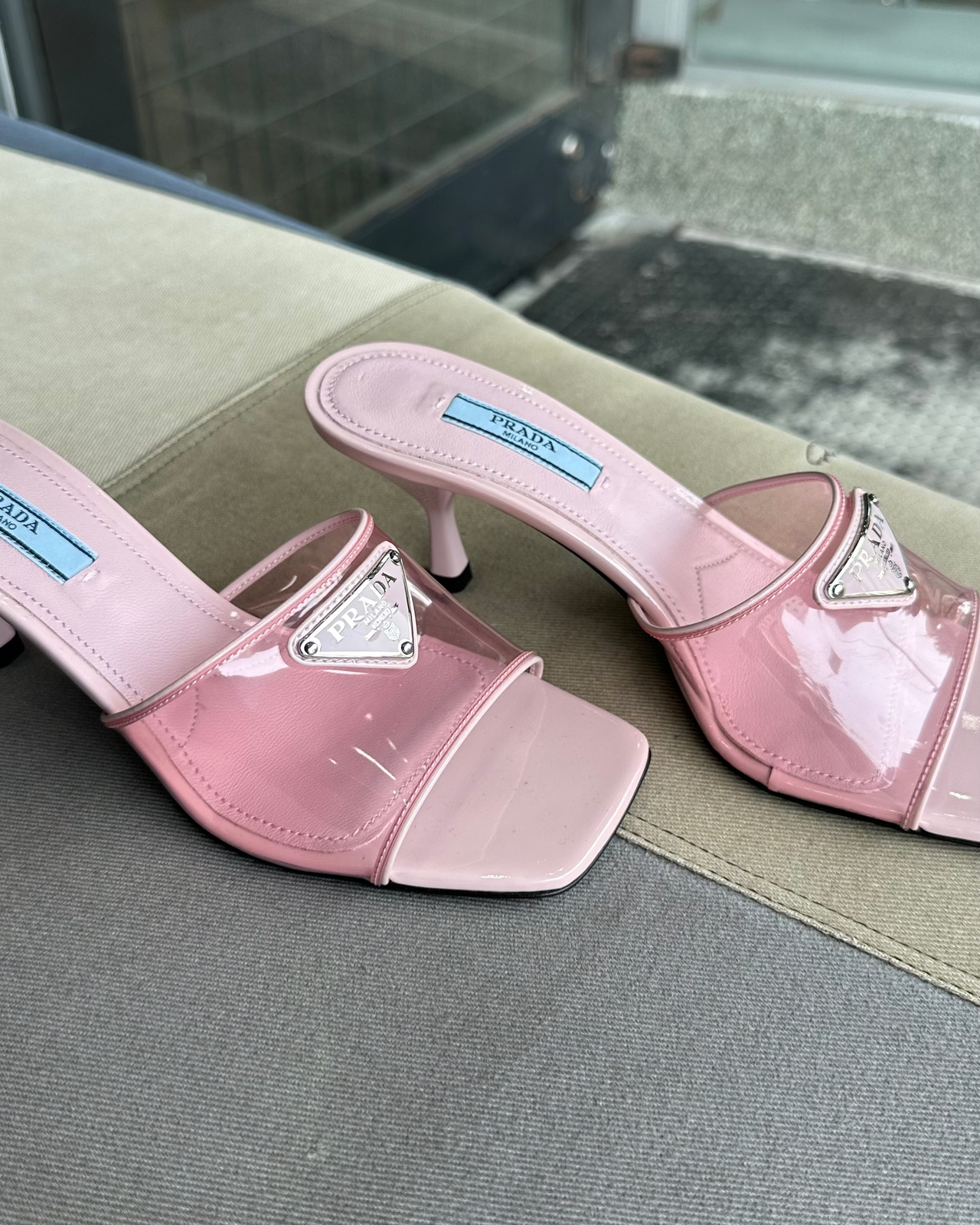 Pink high-heeled Prada shoe on a textured surface with a gray background