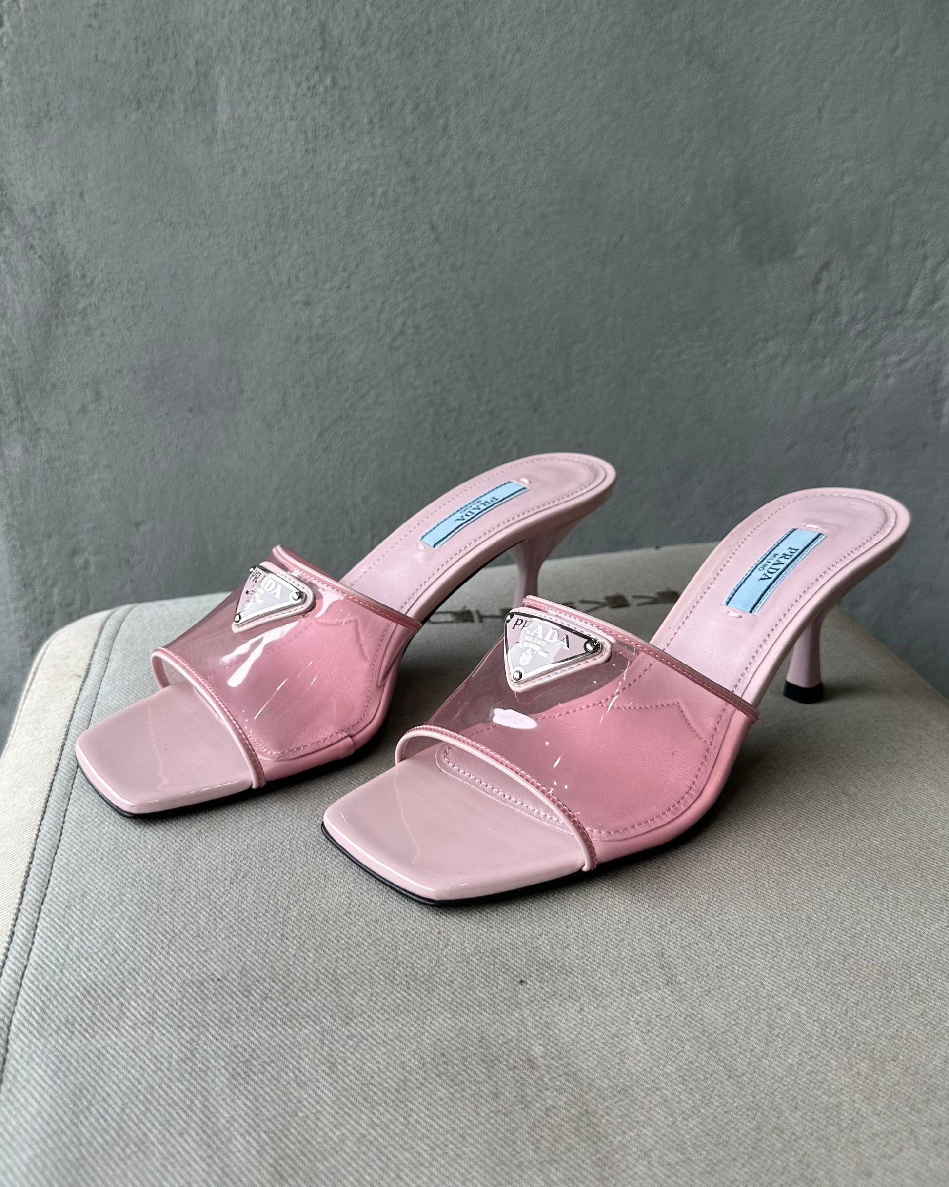 Pair of pink high-heeled Prada shoes with clear straps on a gray surface.