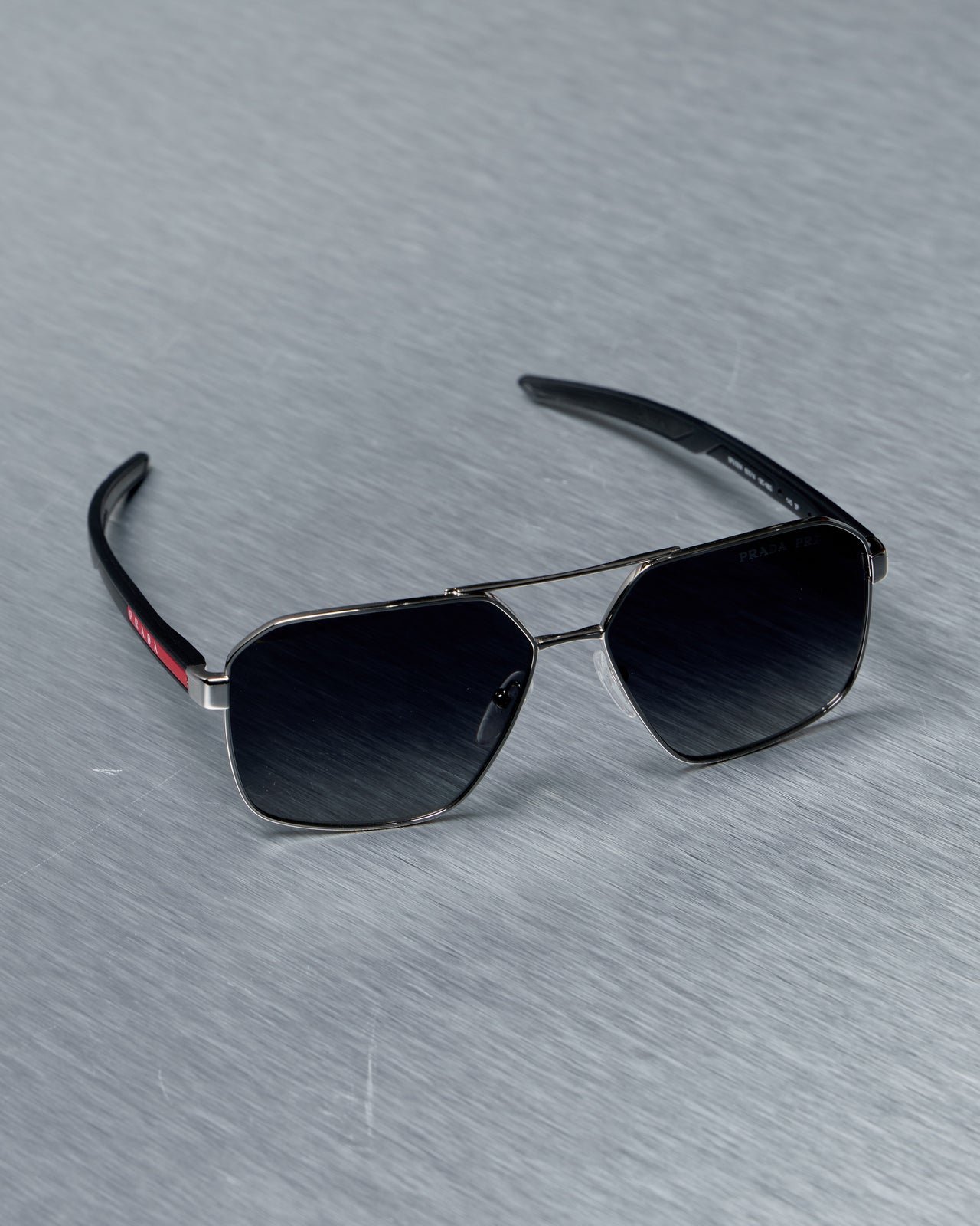 Prada Sunglasses with black lenses and silver frame on a gray textured background