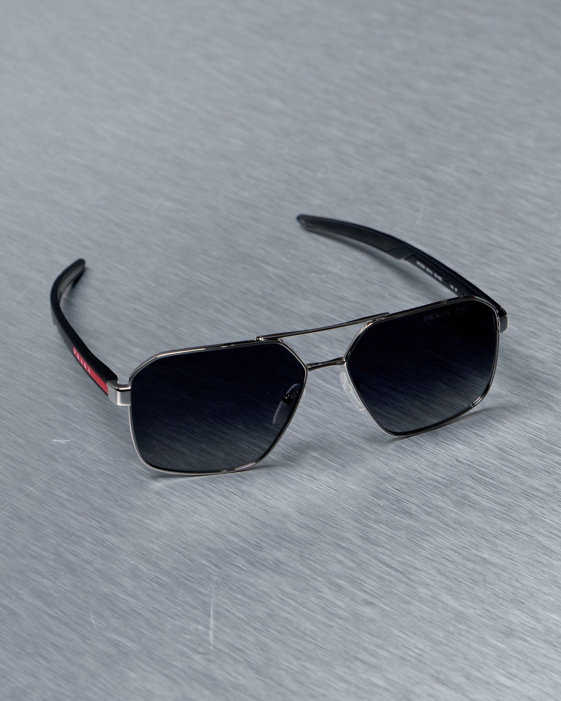 Prada Sunglasses with black lenses and silver frame on a gray textured background