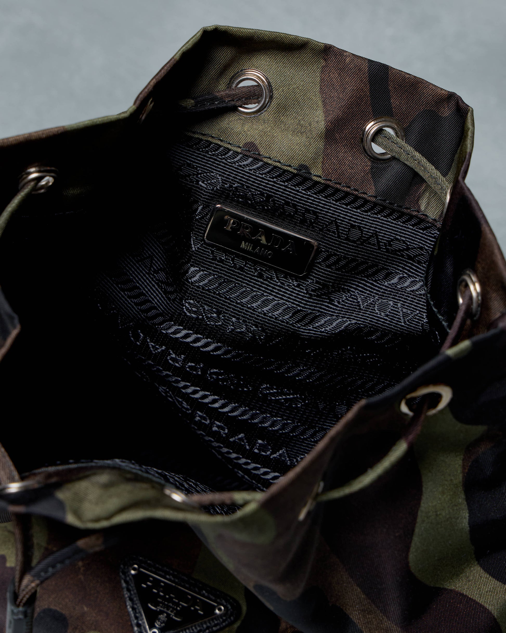 Close-up of a camouflage Prada bag with a brand label on a gray background