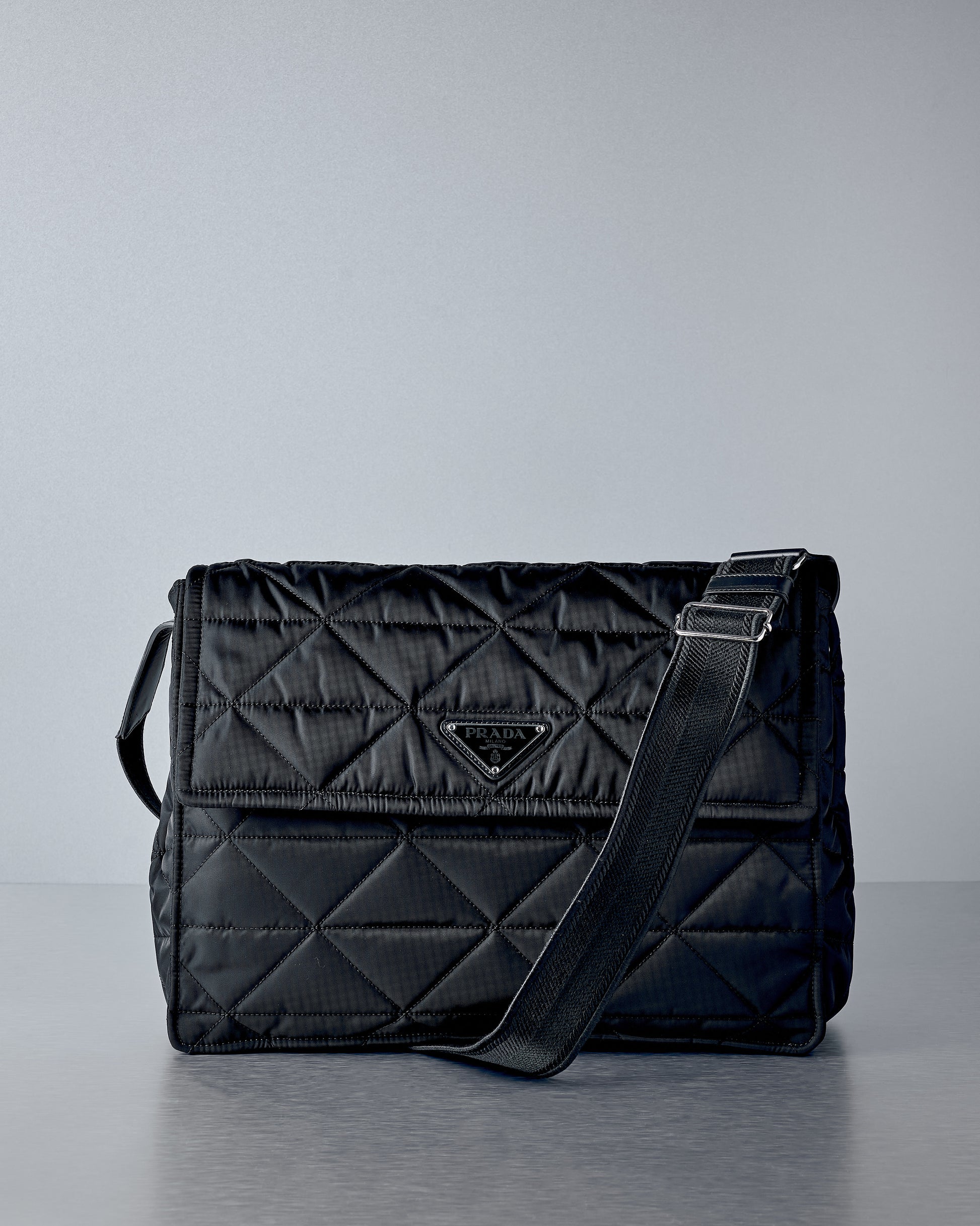 Black quilted handbag with Prada logo on a grey background