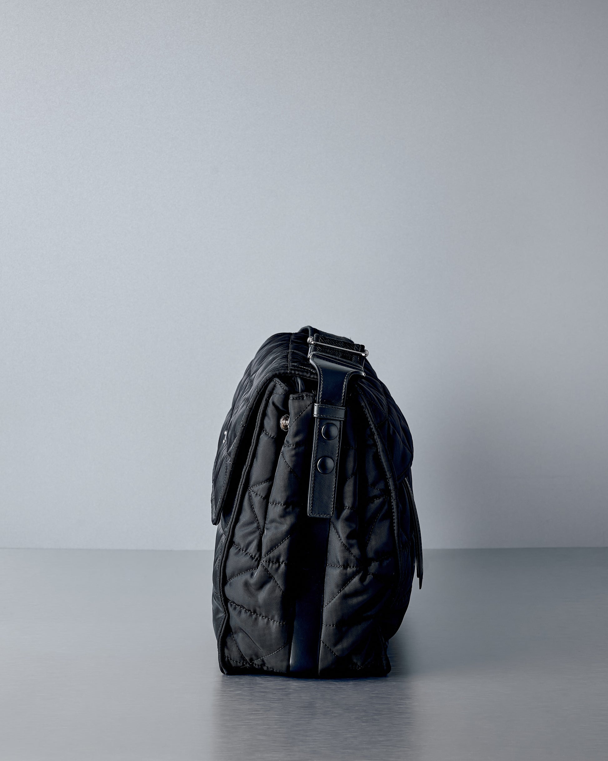 Black Prada messenger bag on a grey surface with a light grey background