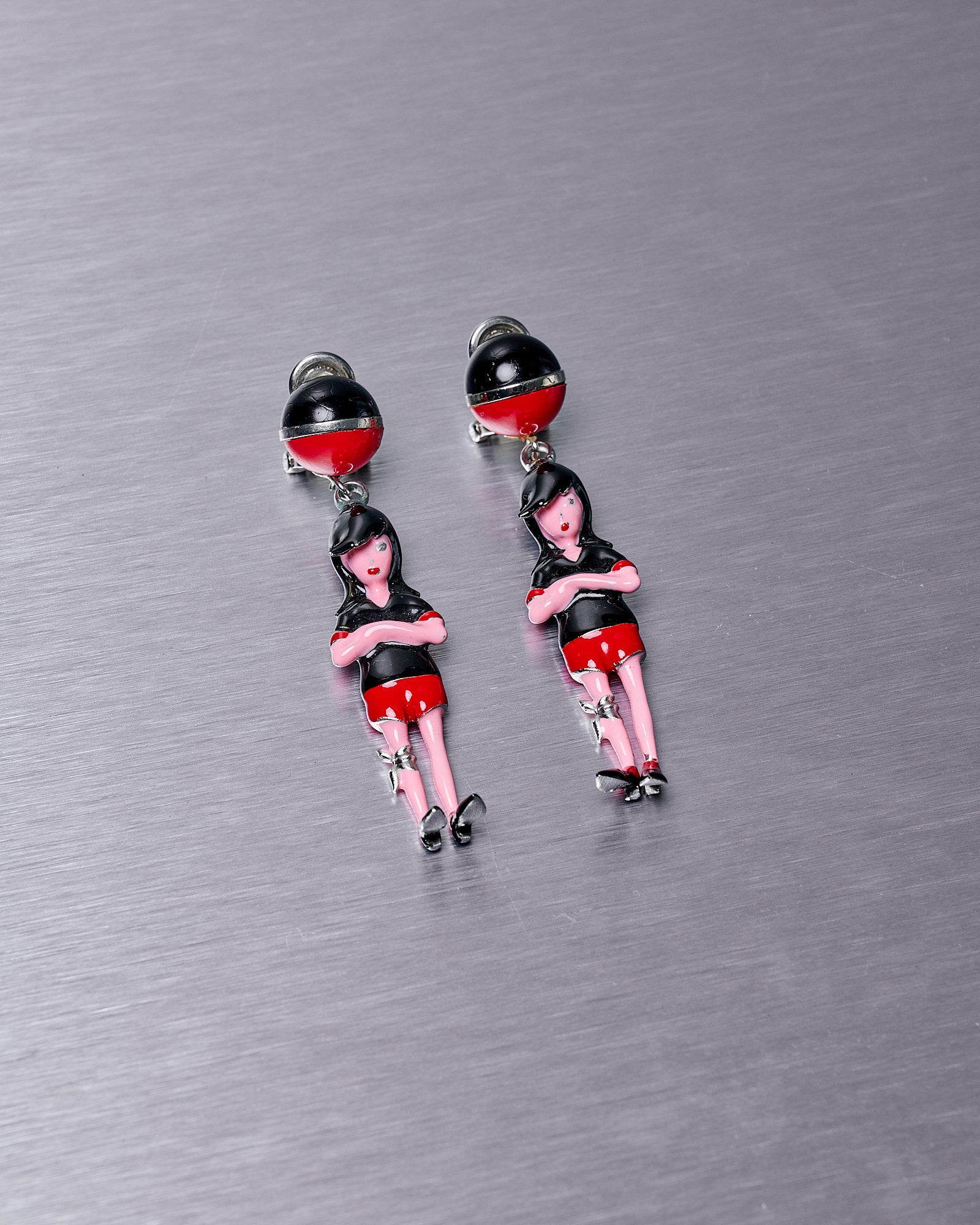 A pair of Prada branded enamel pop rock 3D girl earrings featuring a mod-inspired figurative drop pendant with bandaged knee detailing in red, black, and white colors.