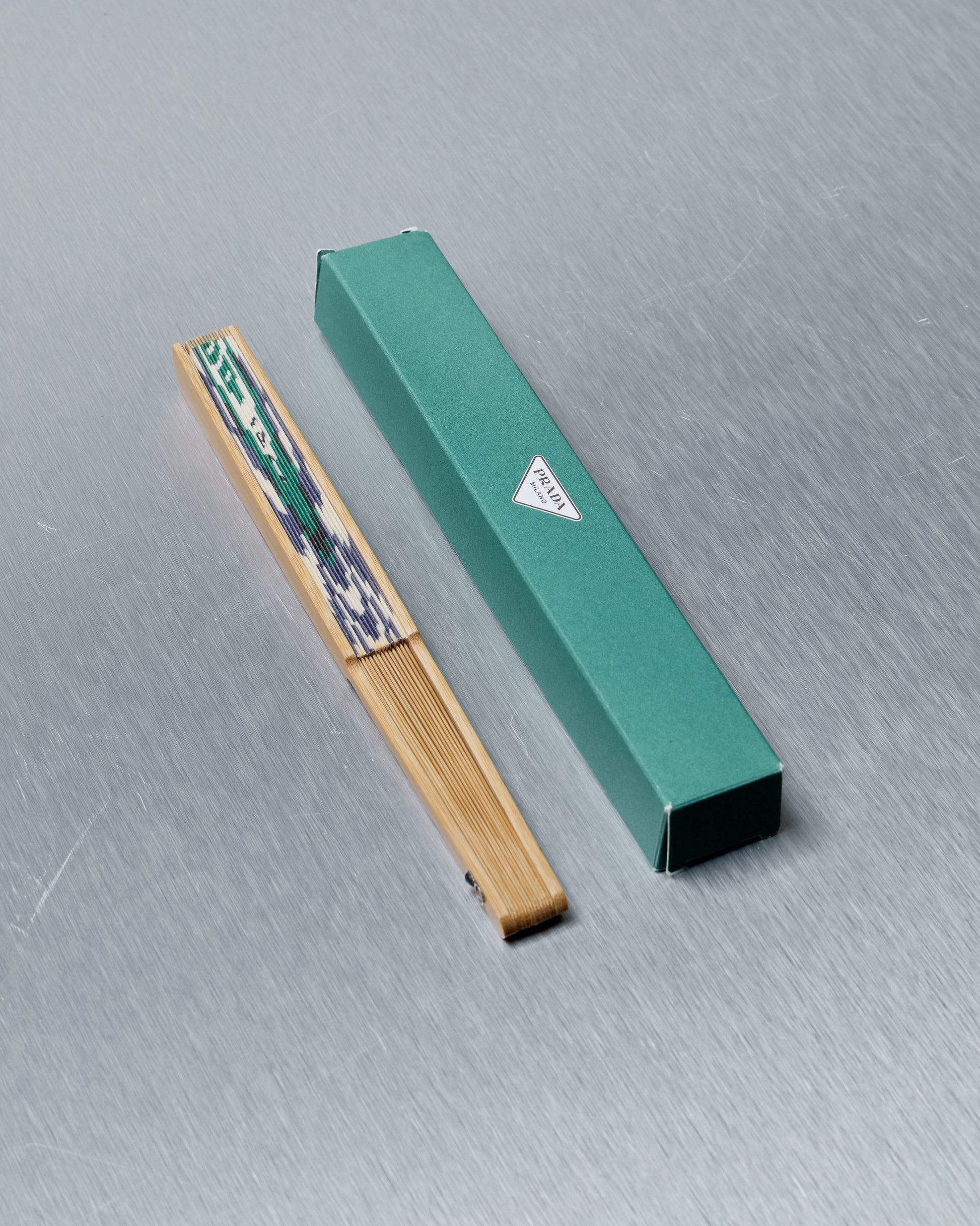 Green packaging Prada box with a wooden item on a gray surface