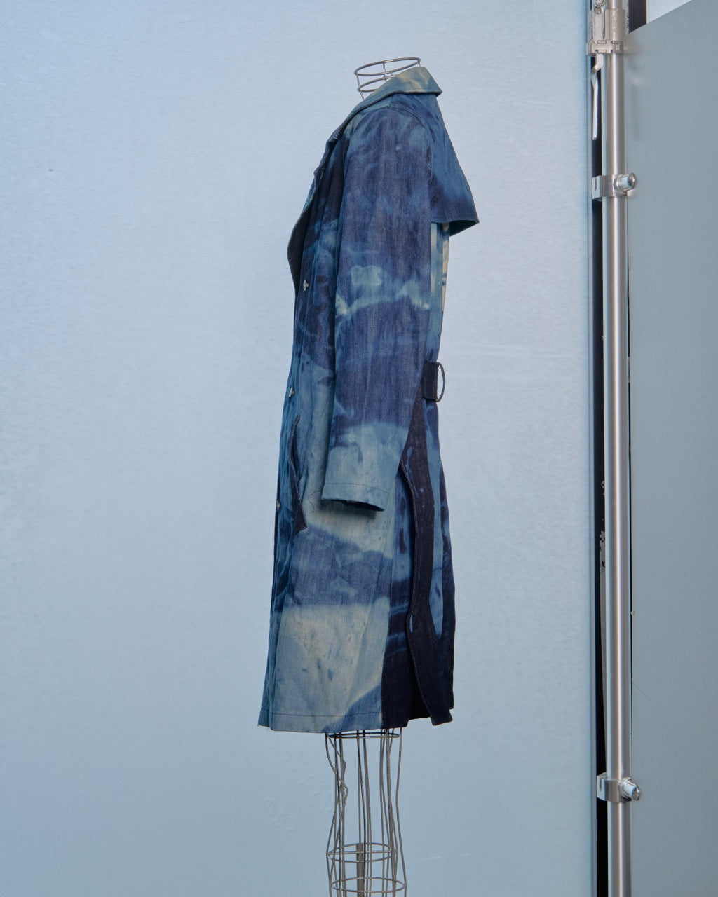 Blue tie-dye Raf Simons trench coat on a mannequin against a light blue wall