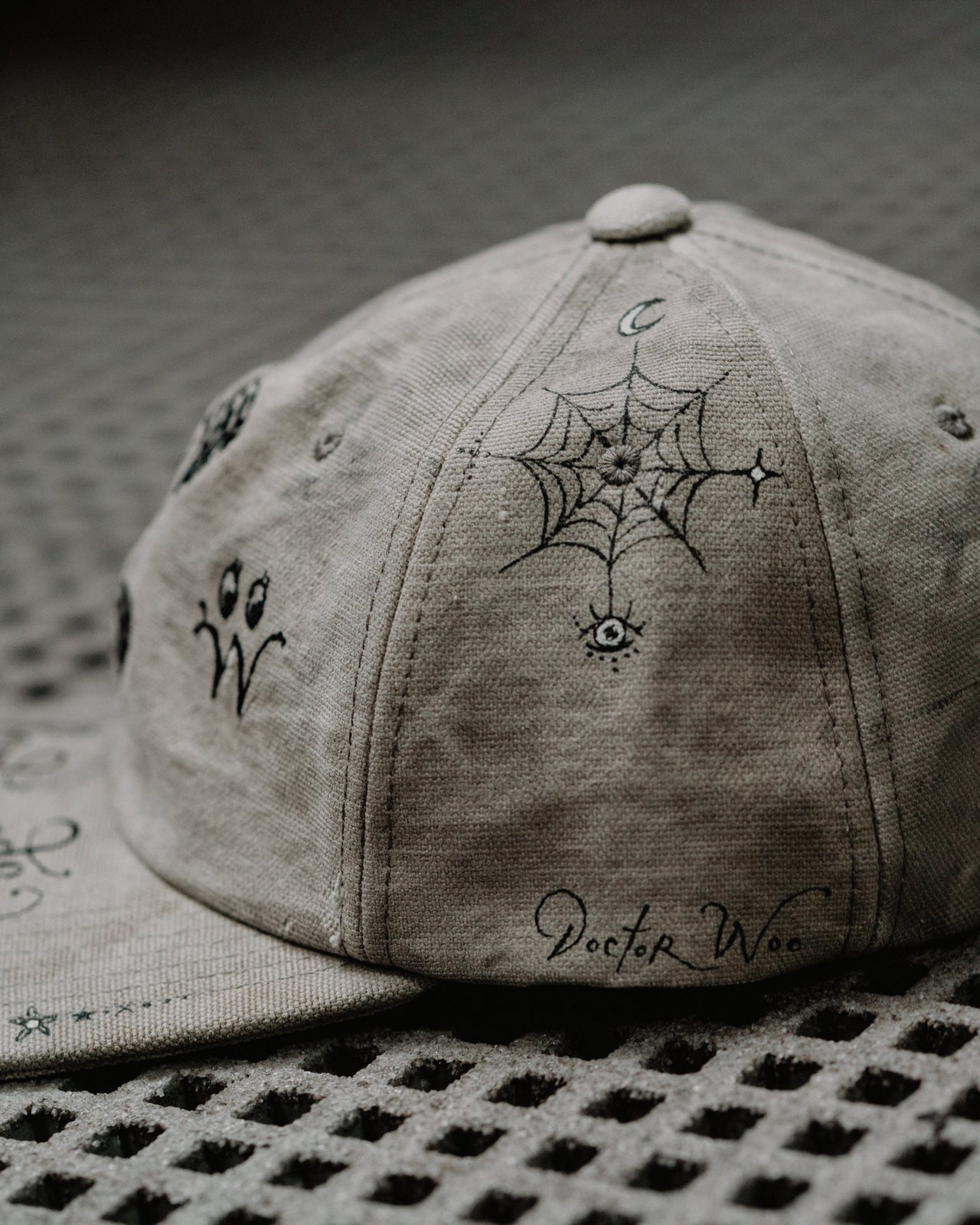 A beige distressed baseball Readymade x Dr Woo cap with a graphic of a skull and crossbones on the front and the brand name 'Readymade' written in a cursive script.