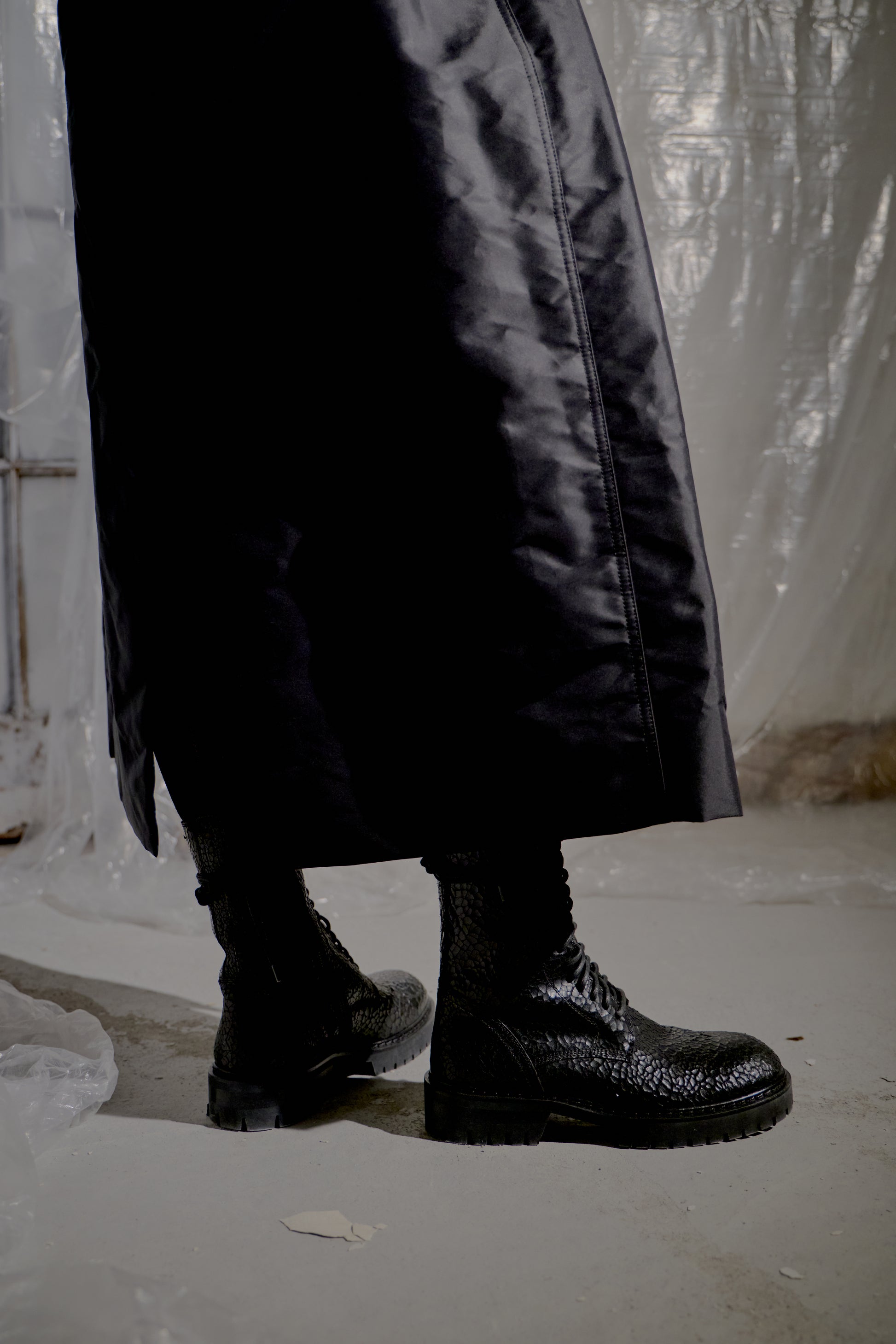 Black boots and a long black Rick Owens coat on a plain background