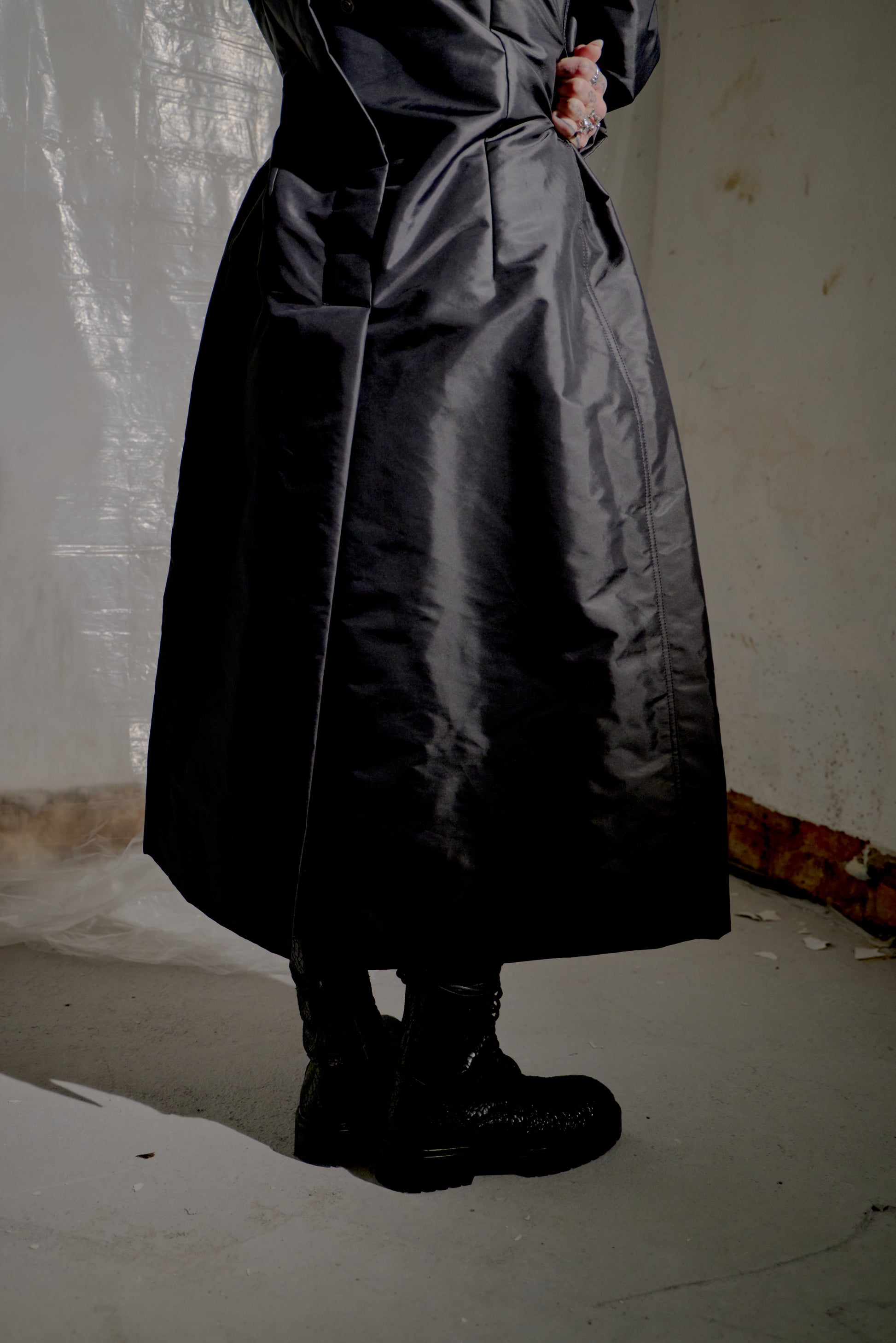 Person wearing a long black Rick Owens coat in a minimal indoor setting