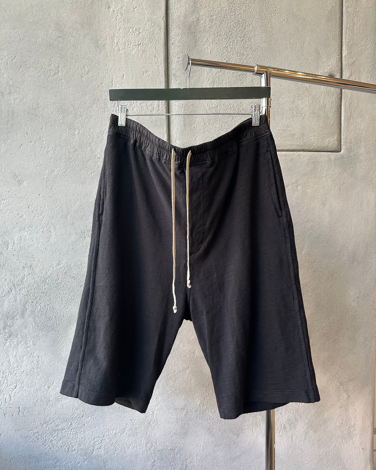 Black Rick Owens shorts on a hanger against a gray wall