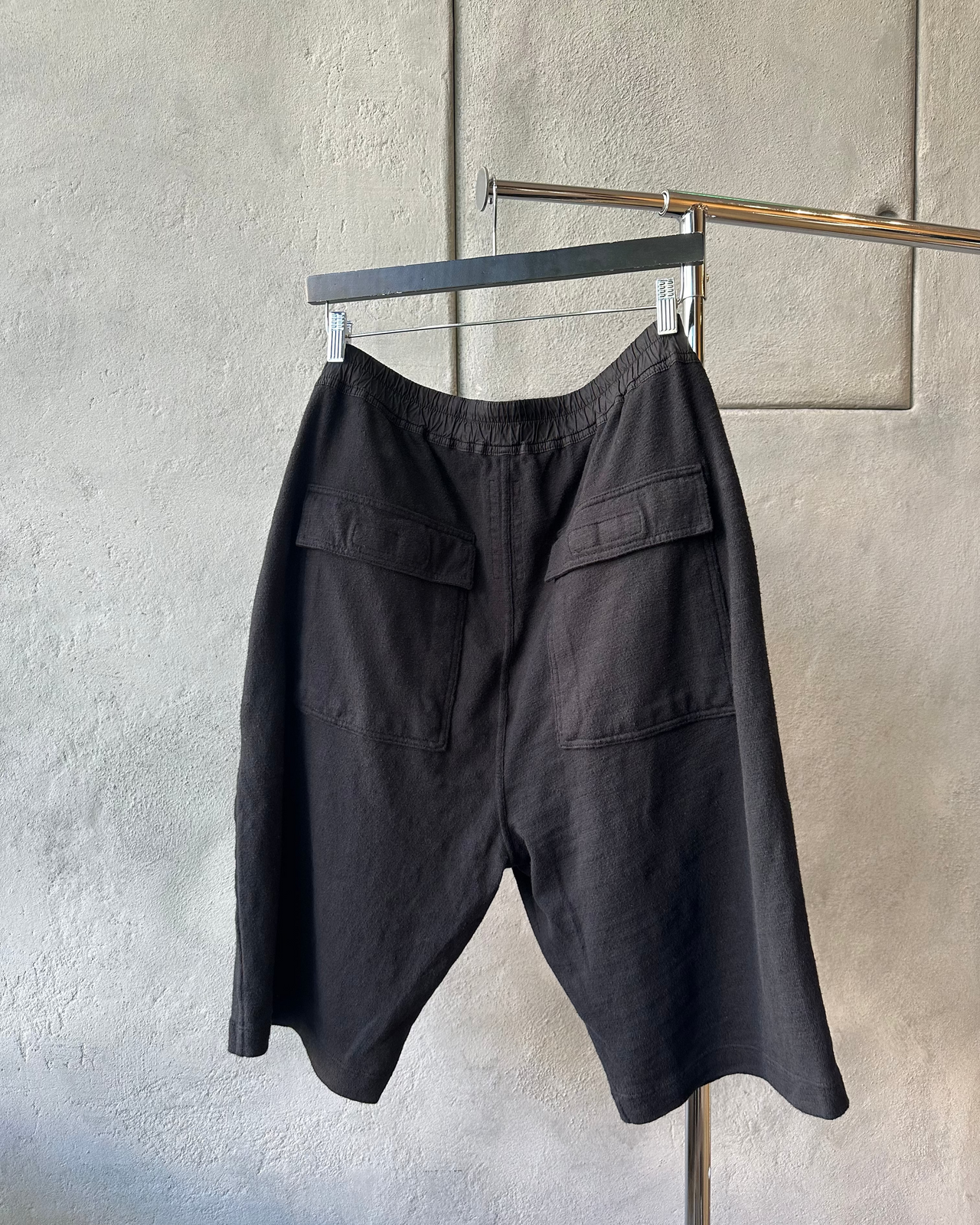 Black Rick Owens shorts on a hanger against a gray wall