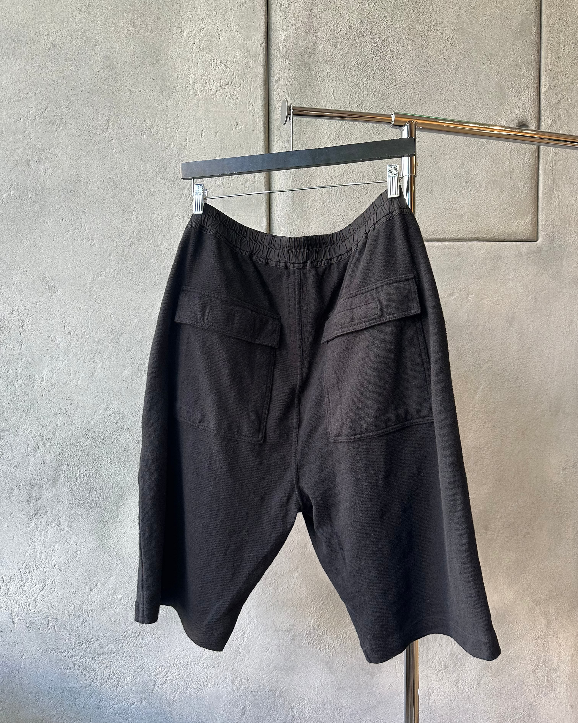 Black Rick Owens shorts hanging on a rack against a gray wall