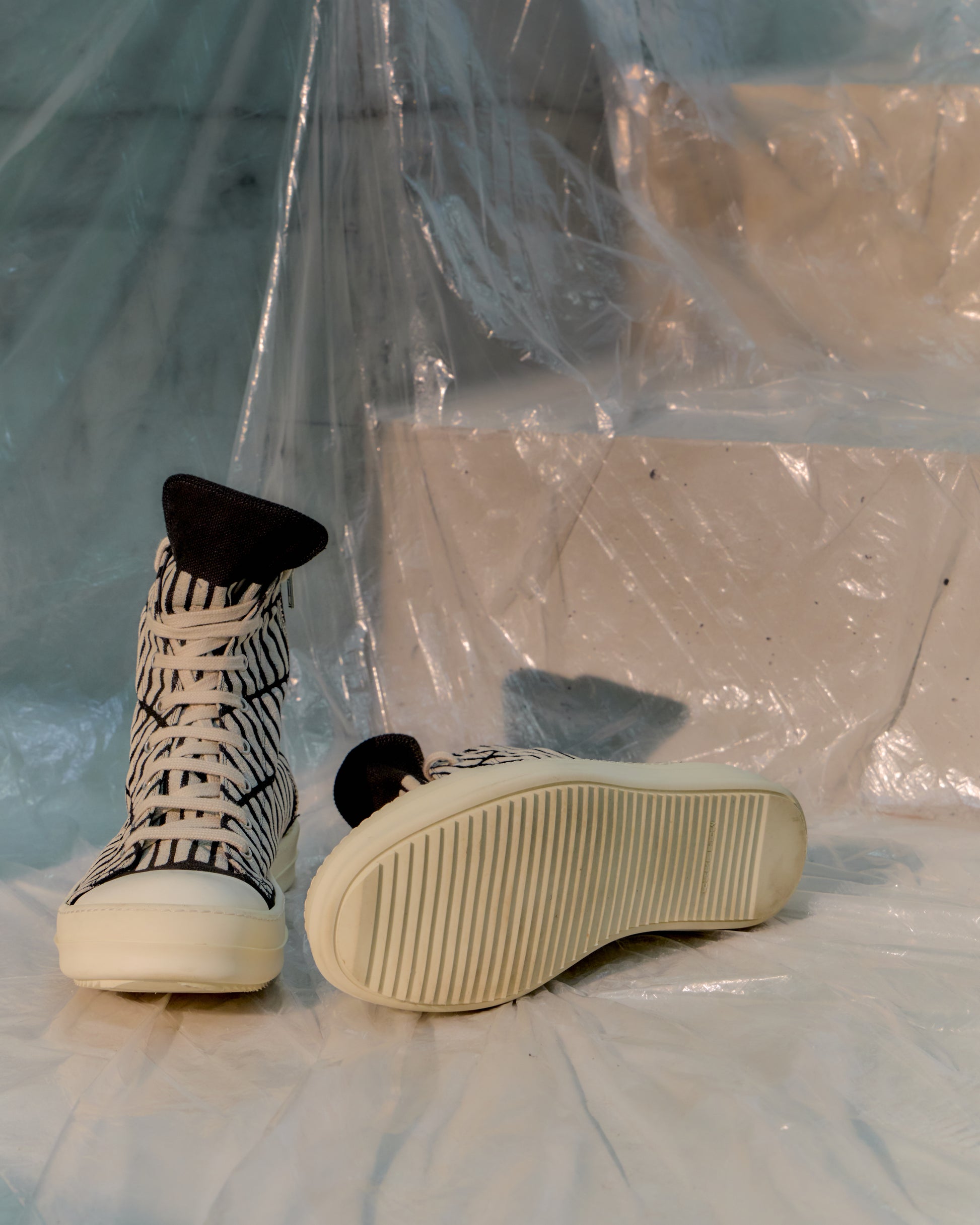 Pair of white Rick Owens sneakers with black soles on a surface covered with plastic sheeting.