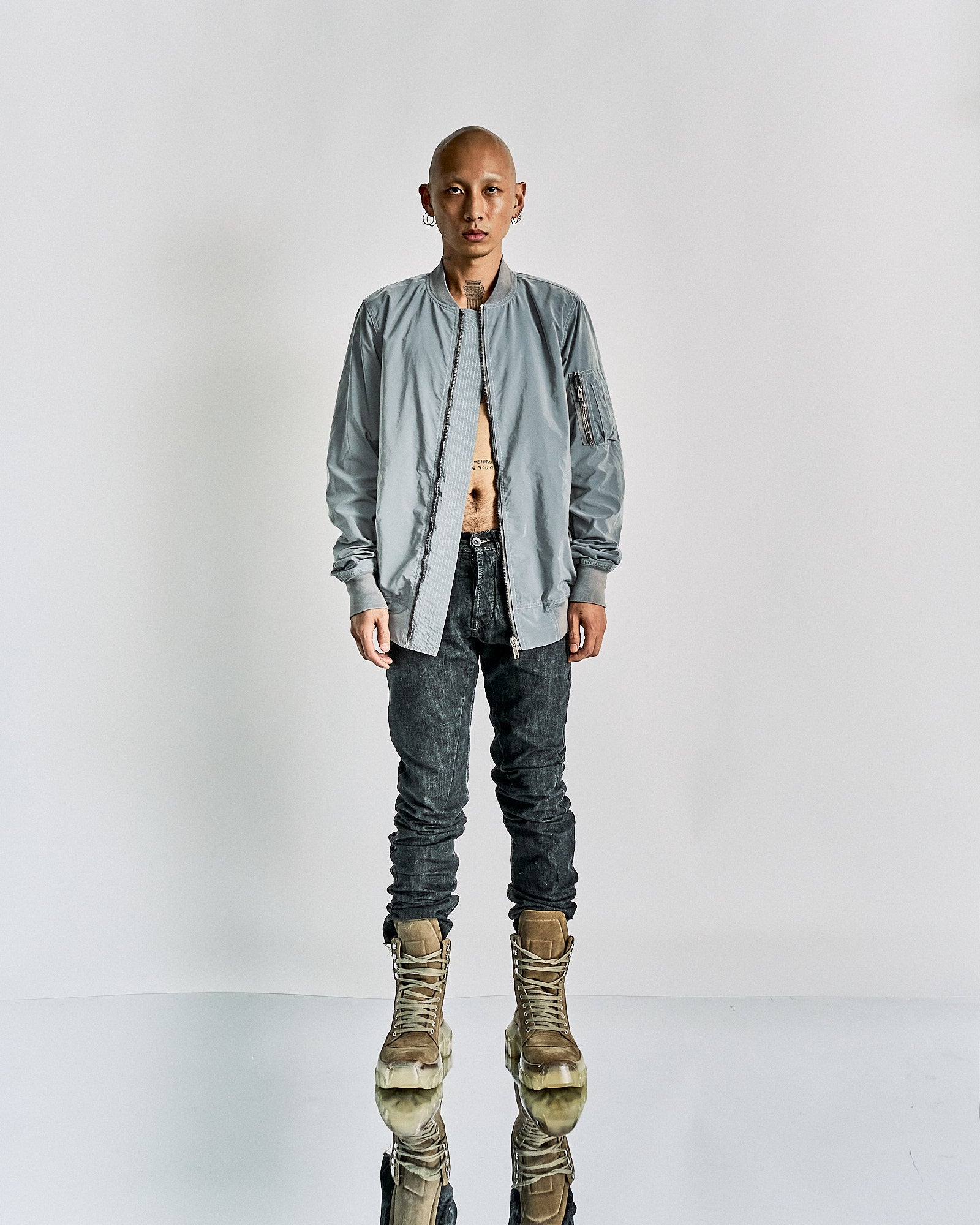 A male model wearing a Rick Owens DRKSHDW SS 2015 bomber jacket in silver, with side pockets and a zip pouch on sleeve, standing against a white background.