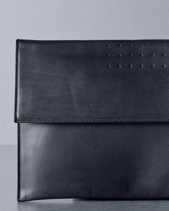 Black leather Rick Owens clutch bag on a gray surface with a light gray background