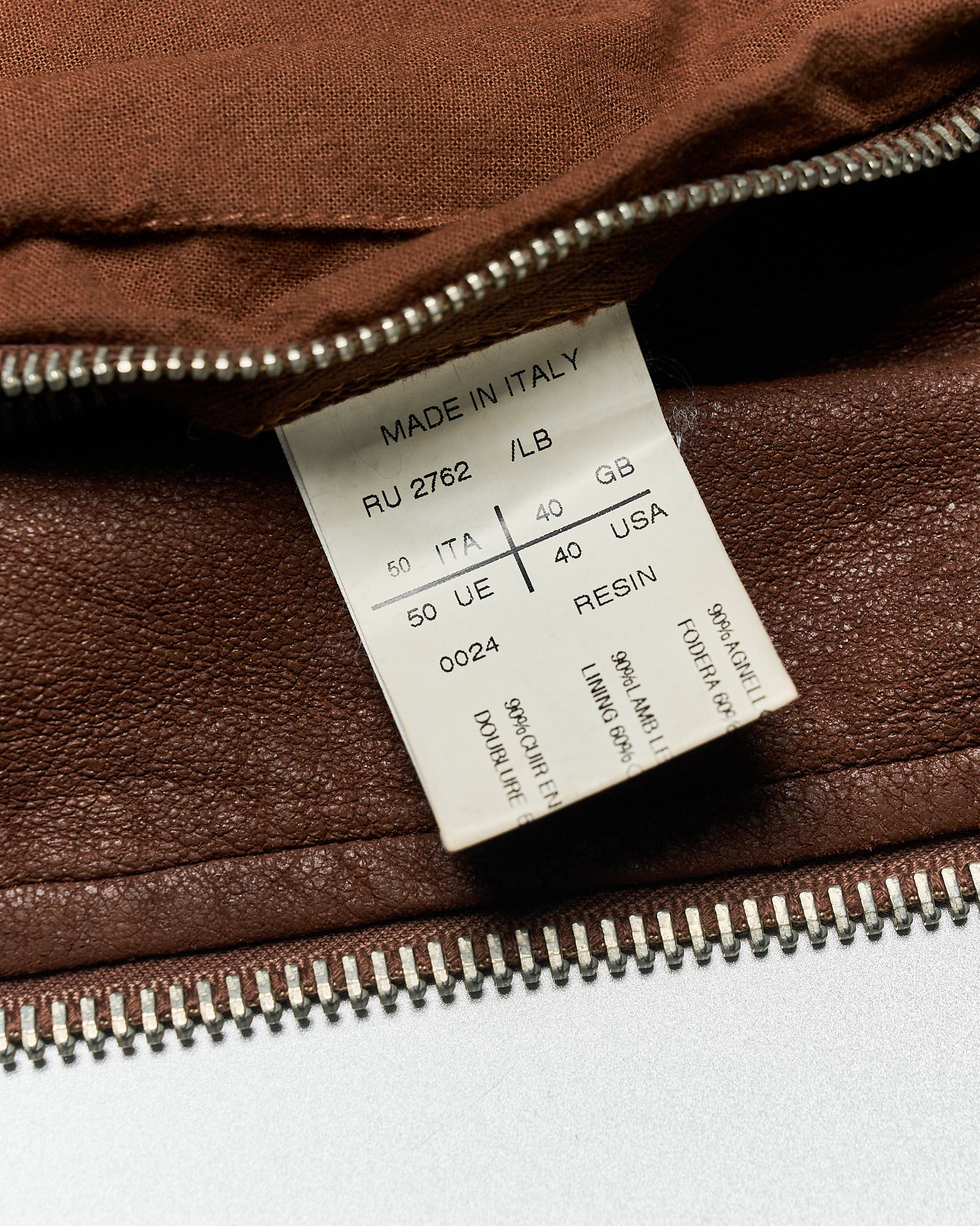 Close-up of a brown leather Rick Owens jacket with a visible label reading “Made in Italy.” The jacket's zipper is unzipped, revealing the label, which lists sizes and materials.