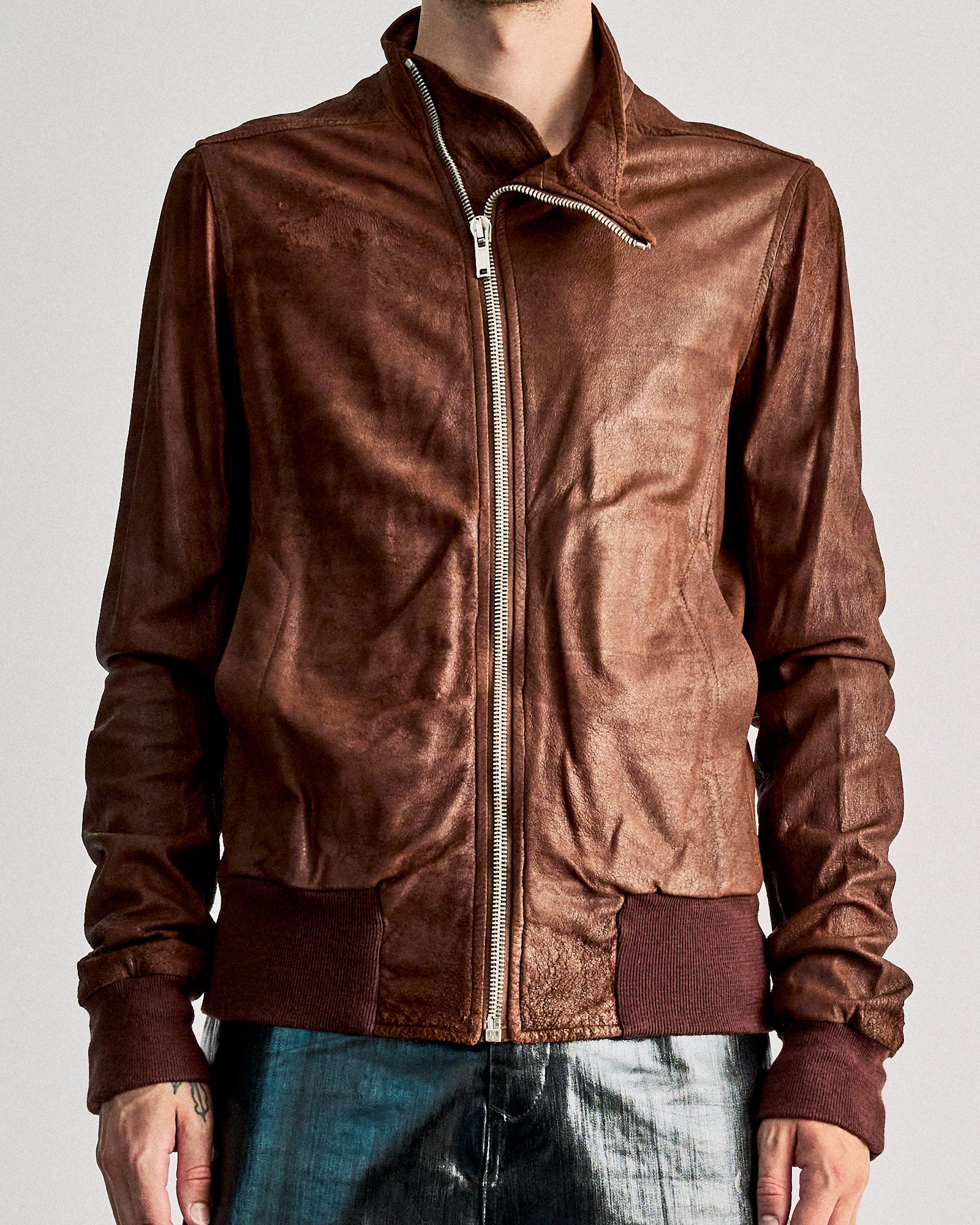 Man wearing a brown leather Rick Owens jacket with a high collar and full zipper, paired with metallic pants. 