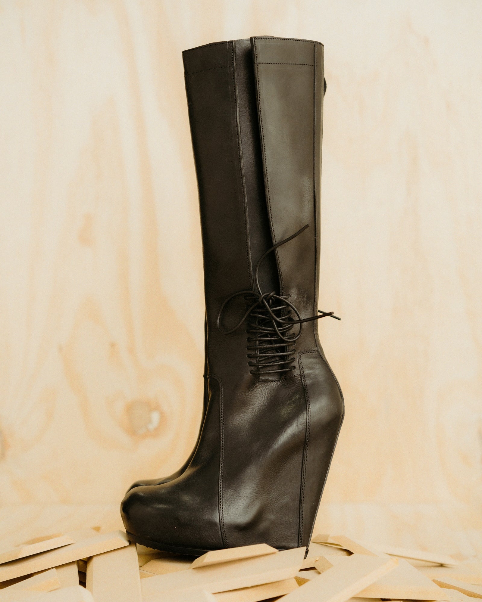 Black leather knee-high Rick Owens boot on a wooden surface