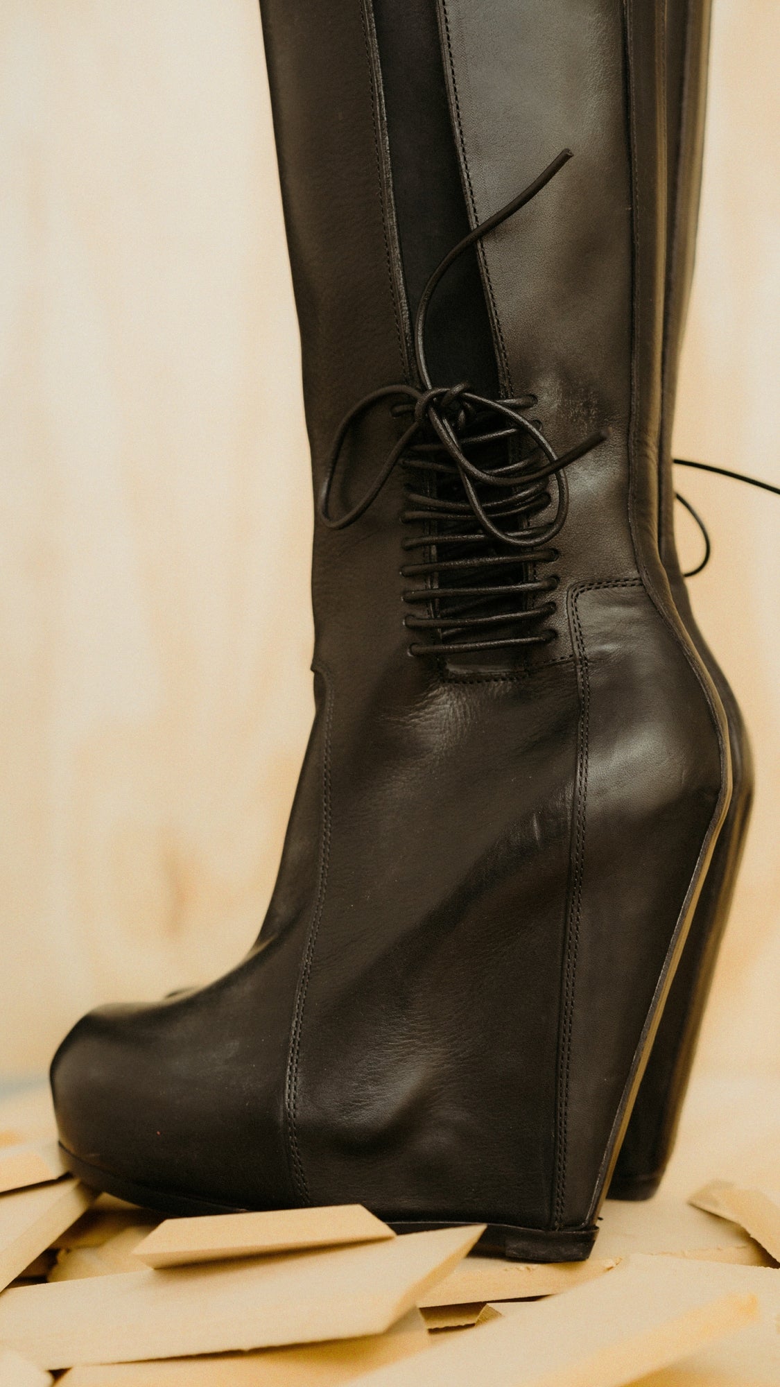 Black leather Rick Owens platform boots with laces on a beige background