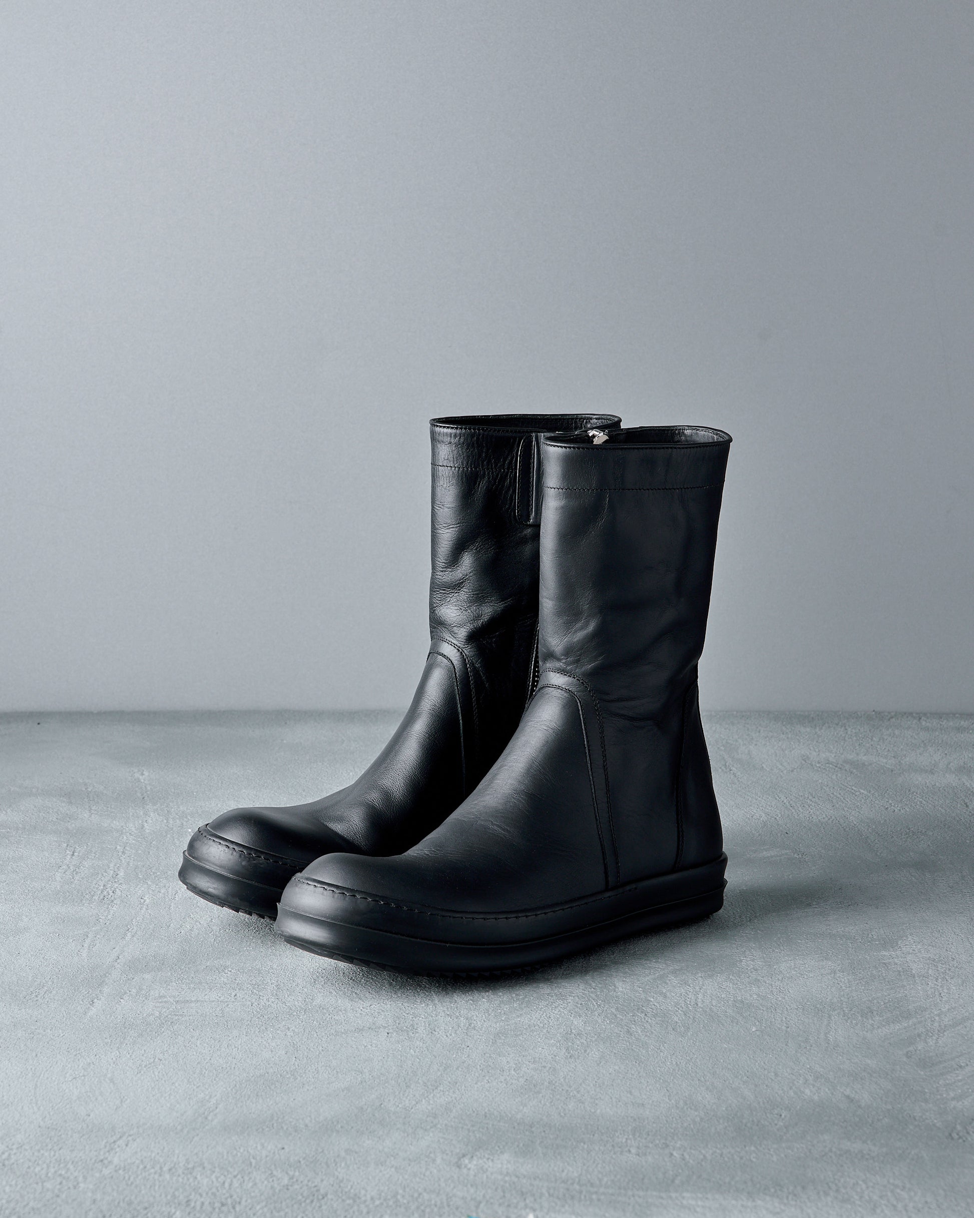 Pair of black leather Rick Owens boots on a gray surface with a gray background