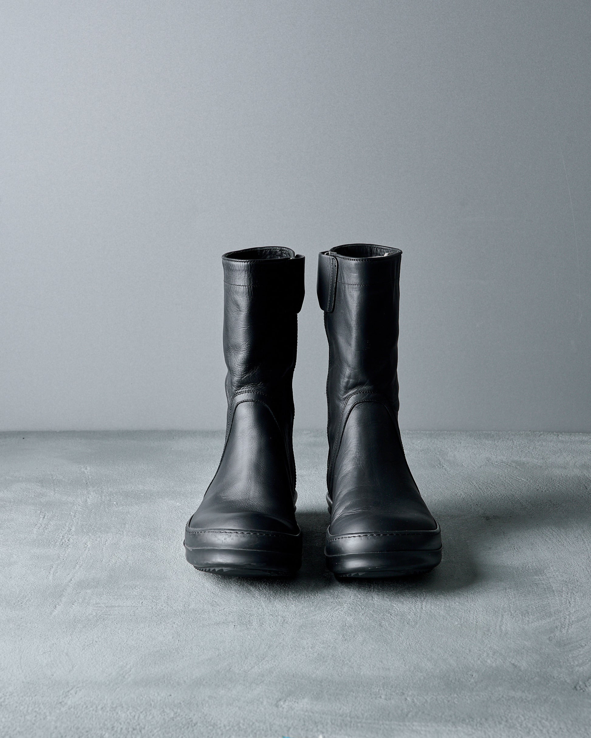 Pair of black leather Rick Owens boots on a gray surface with a gray background