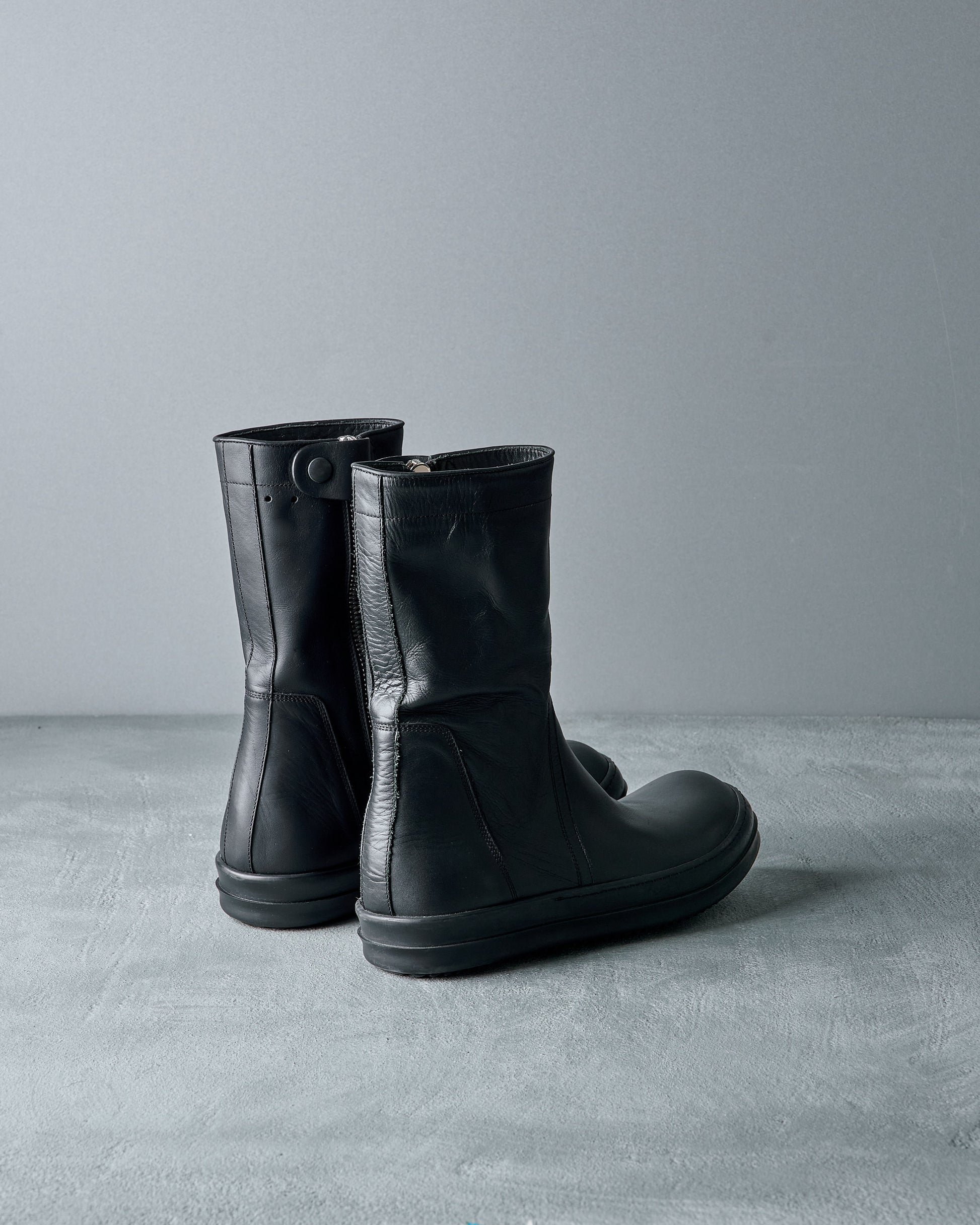 Pair of black Rick Owens rubber and leather boots on a gray surface with a gray background
