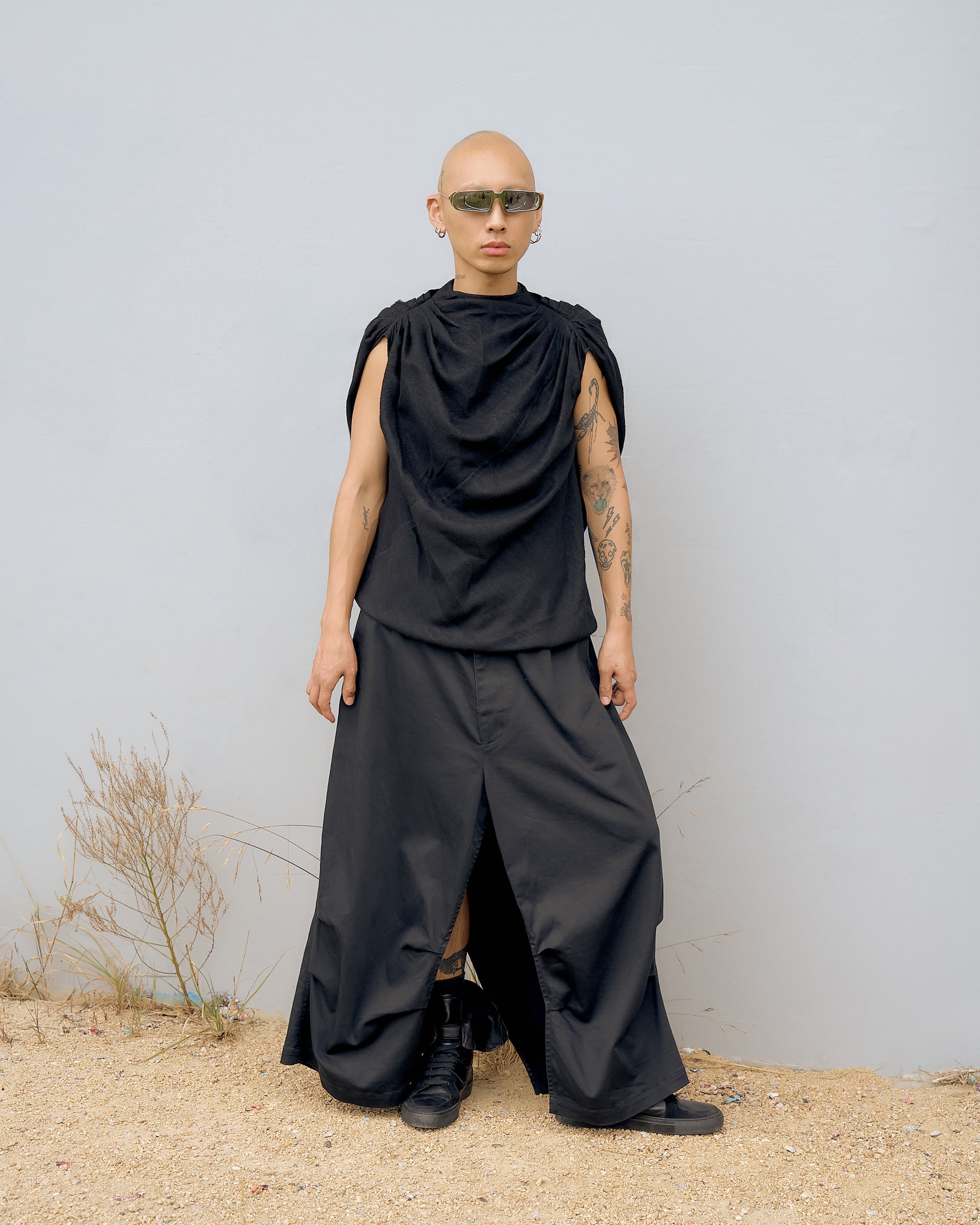 A person wearing a black, bias-cut Rick Owens top with ruched pleating across the shoulders and a tonal back zip with long nylon pull. The individual is standing against a neutral background.