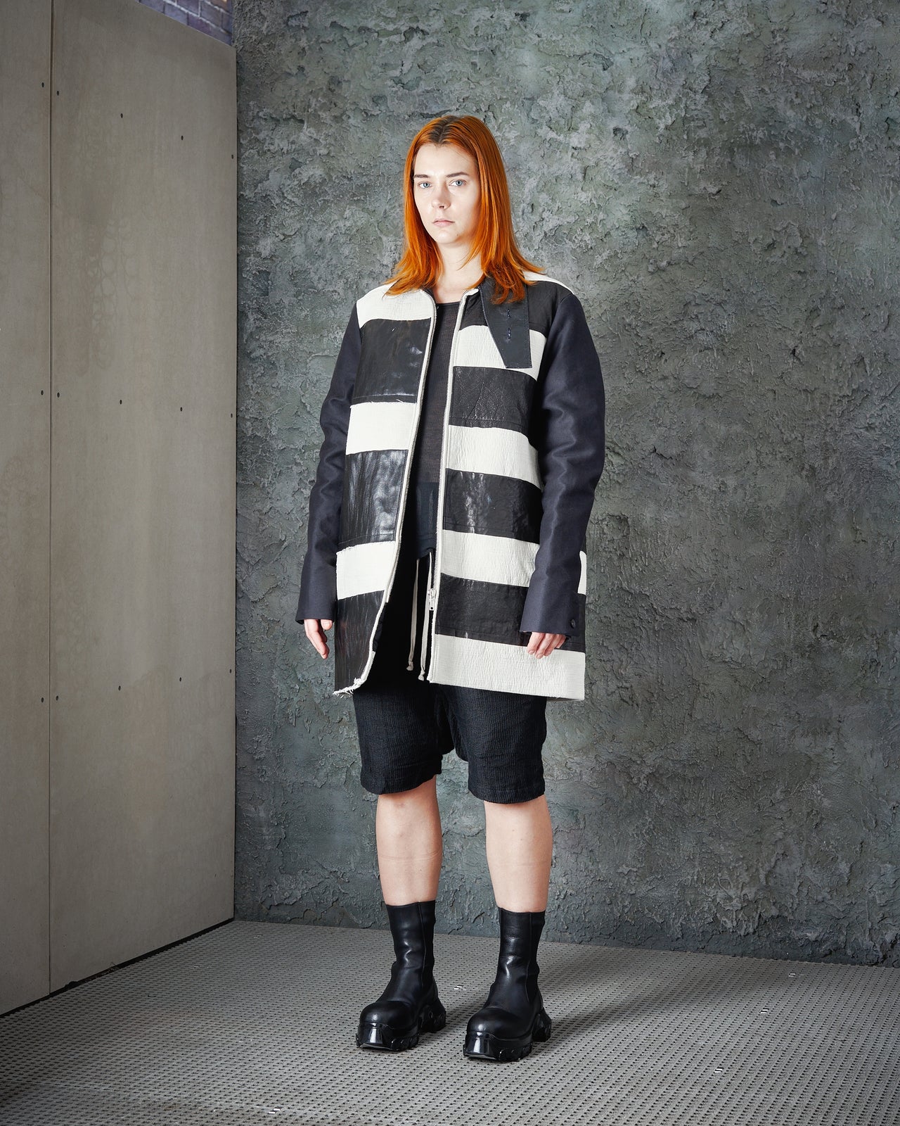 Model in avant-garde fashion walks runway wearing oversized black and white striped Rick Owens jacket with textured leather. Mood is edgy and modern.