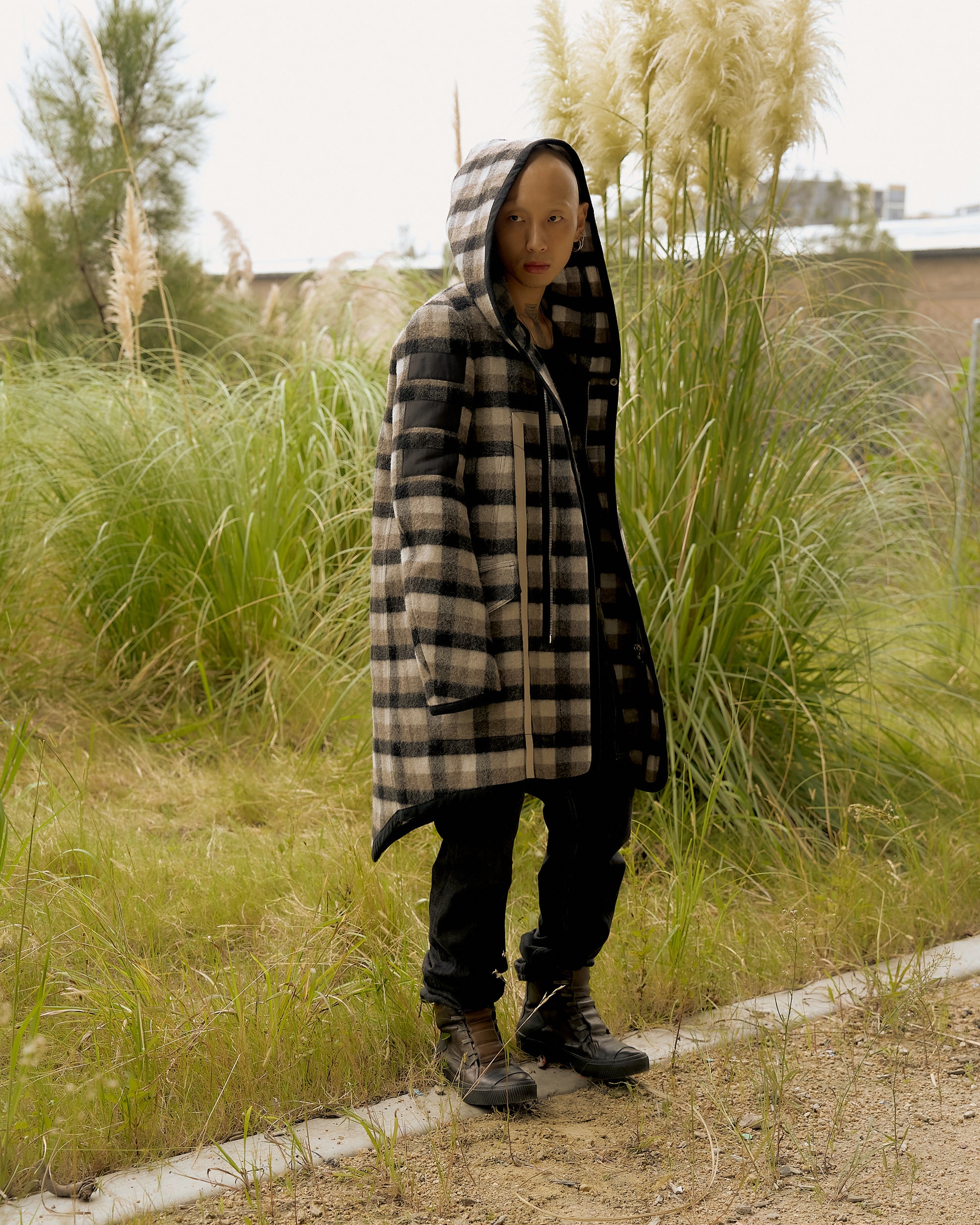 A person standing outdoors wearing a hooded, plaid-patterned Rick Owens coat with a cape-like silhouette.